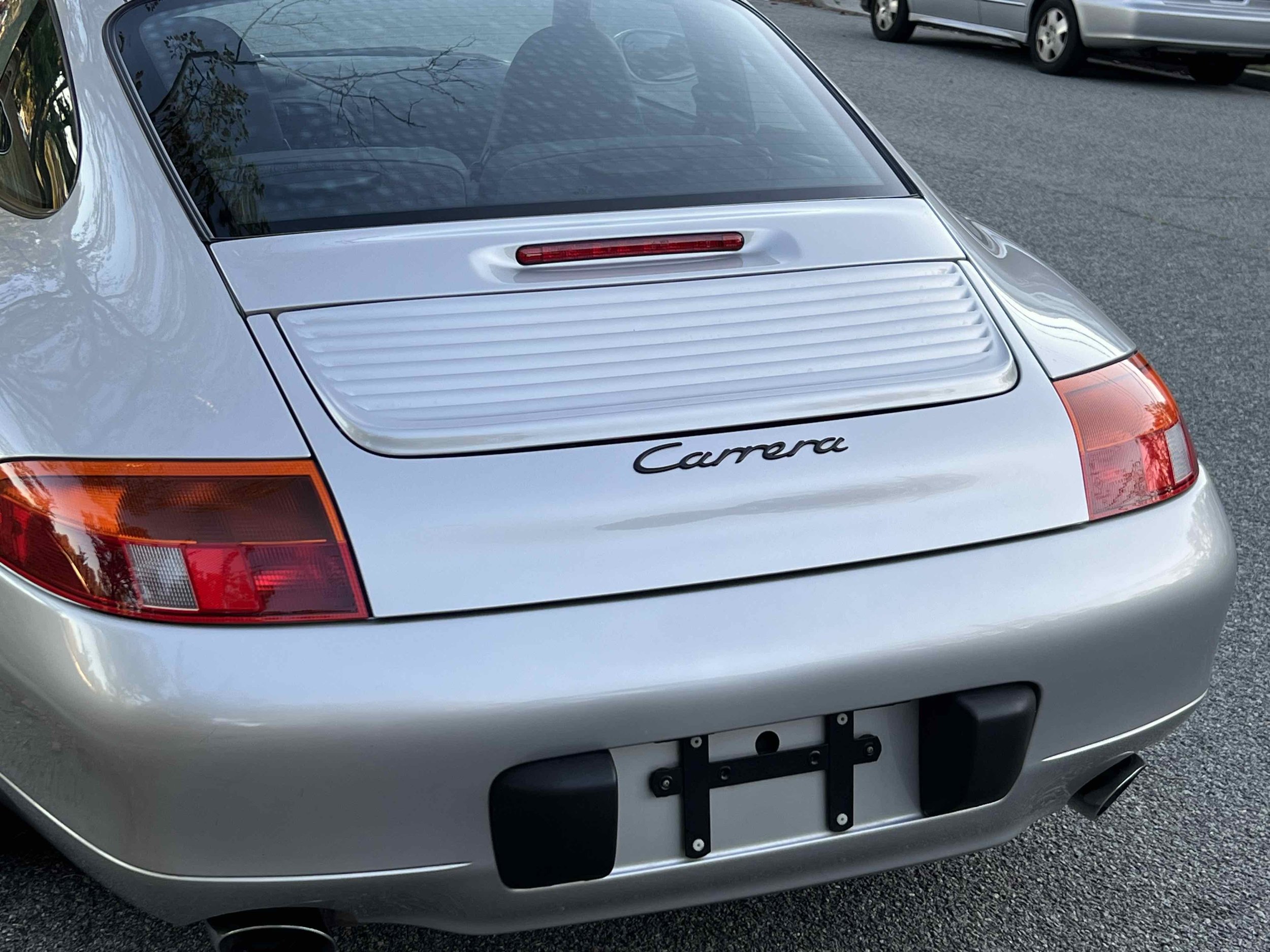 Rear view of a silver Porsche Carrera, showing the car's trunk, taillights, rear bumper, and part of the rear window.