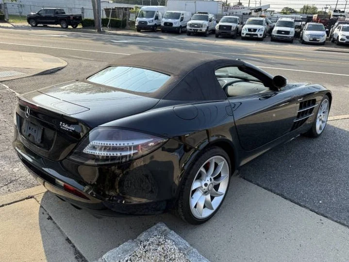 Black Mercedes-Benz convertible sports car parked on street with other vehicles in the background.