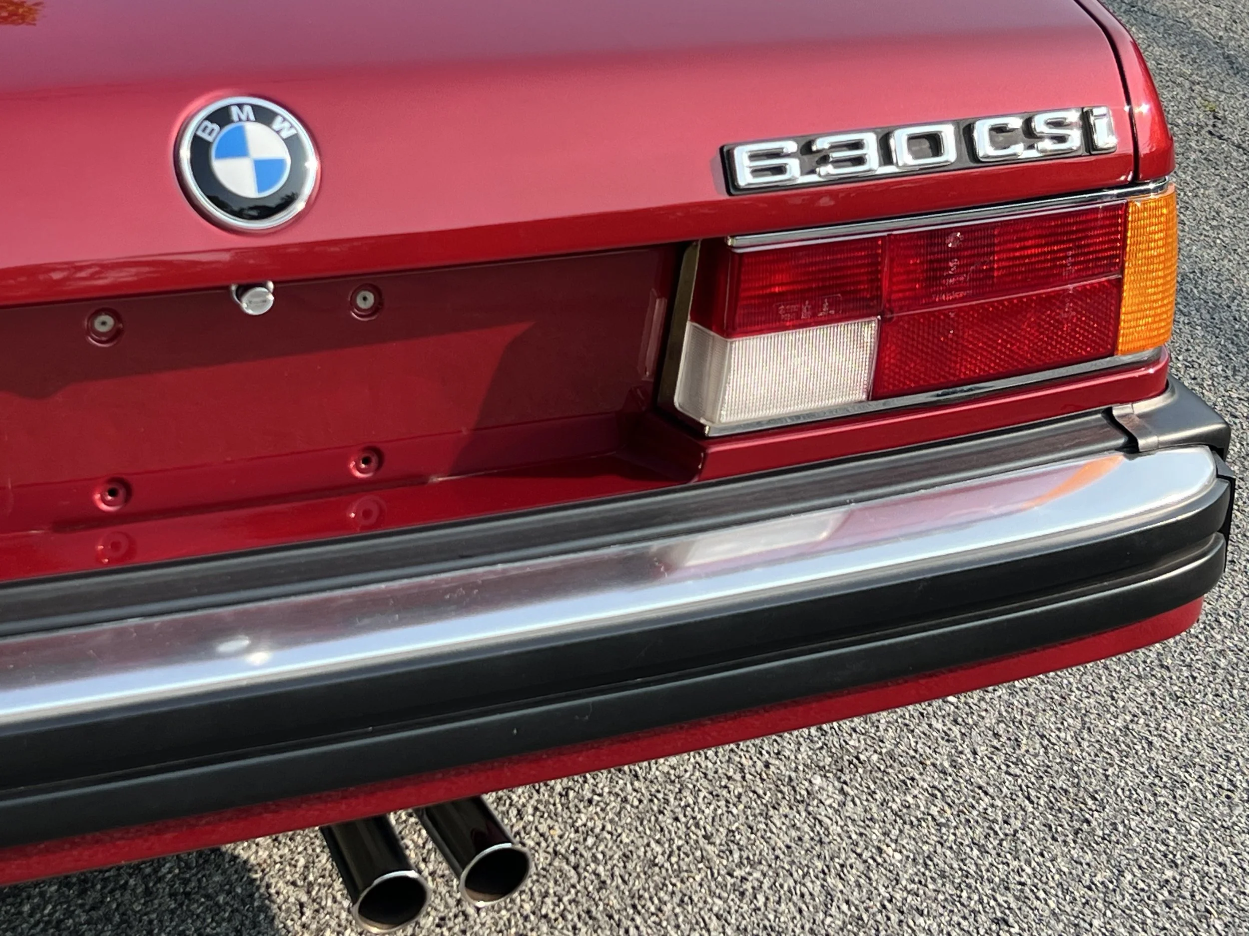 Back of Ruby Red 1977 BMW 630 csi on display in park showing BMW roundel and 630csi badge for sale at FlowHaus