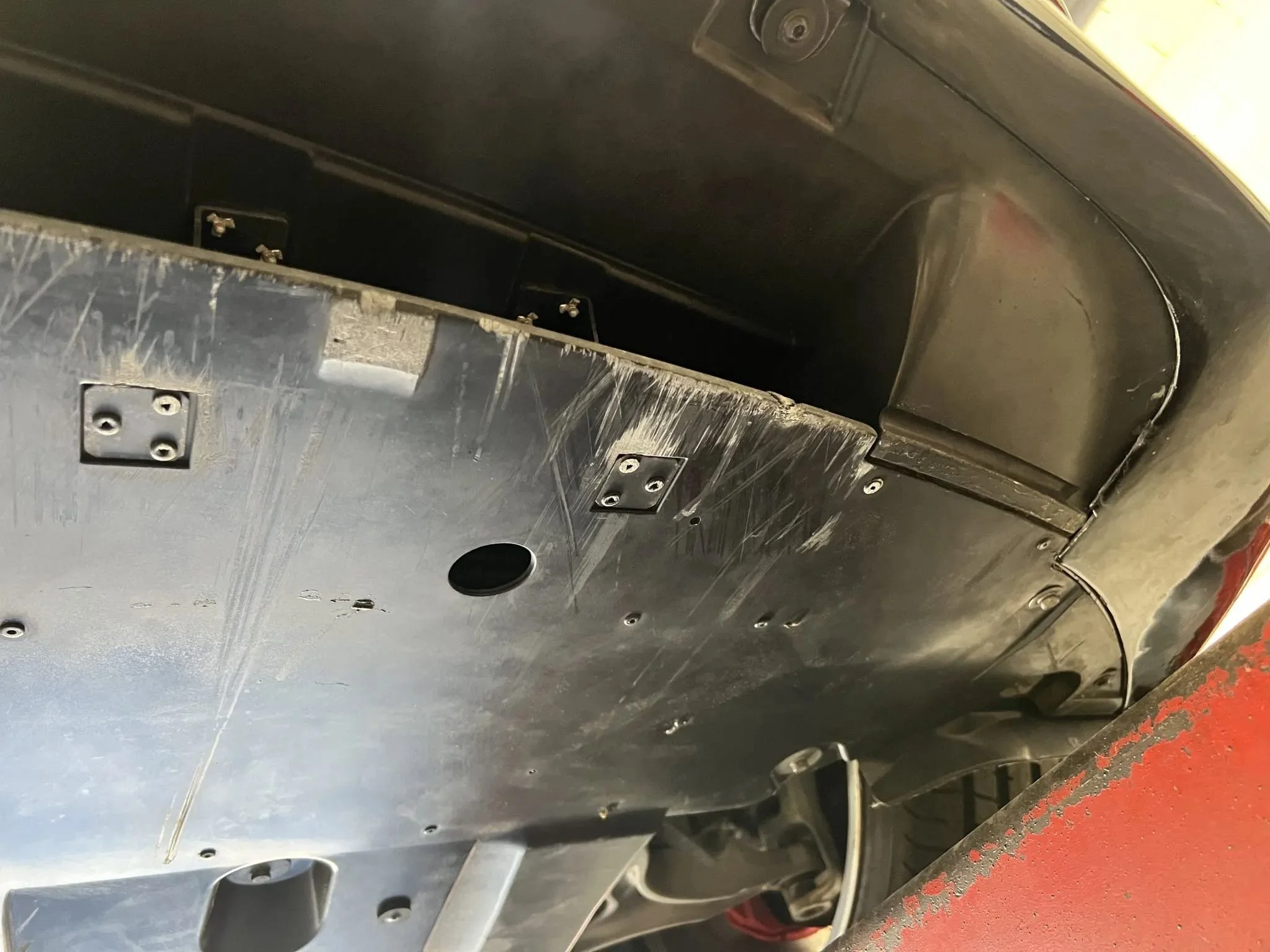 Underneath view of a vehicle with a metal skid plate installed, showing screws and mounting points.