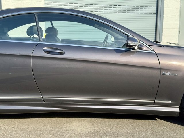 Passenger side of Grey 2008 Mercedes Benz CL63 AMG on pavement with two green garage doors in the background for sale at FlowHaus