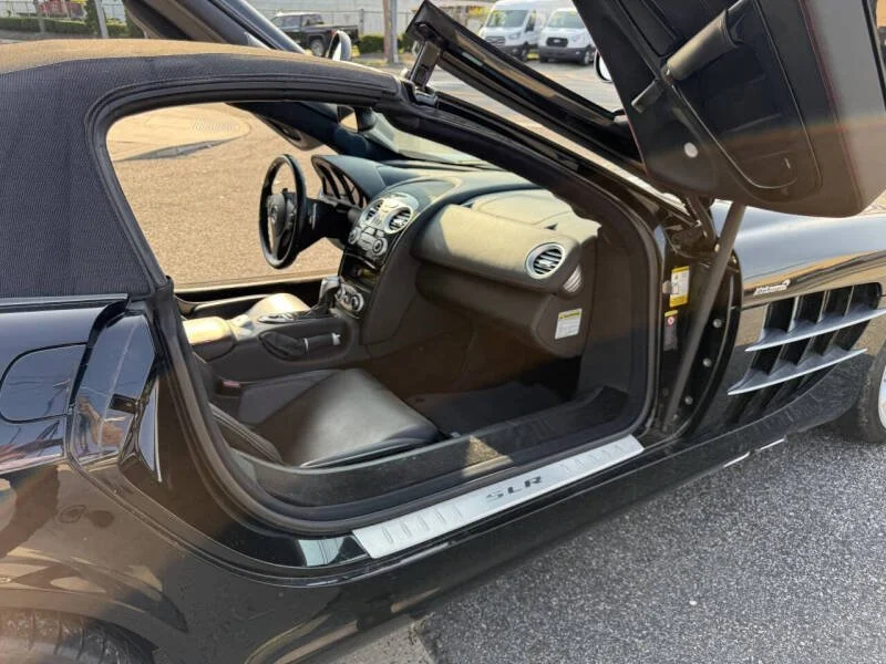 Interior view of a black sports car with gullwing door open, showing the dashboard and steering wheel.