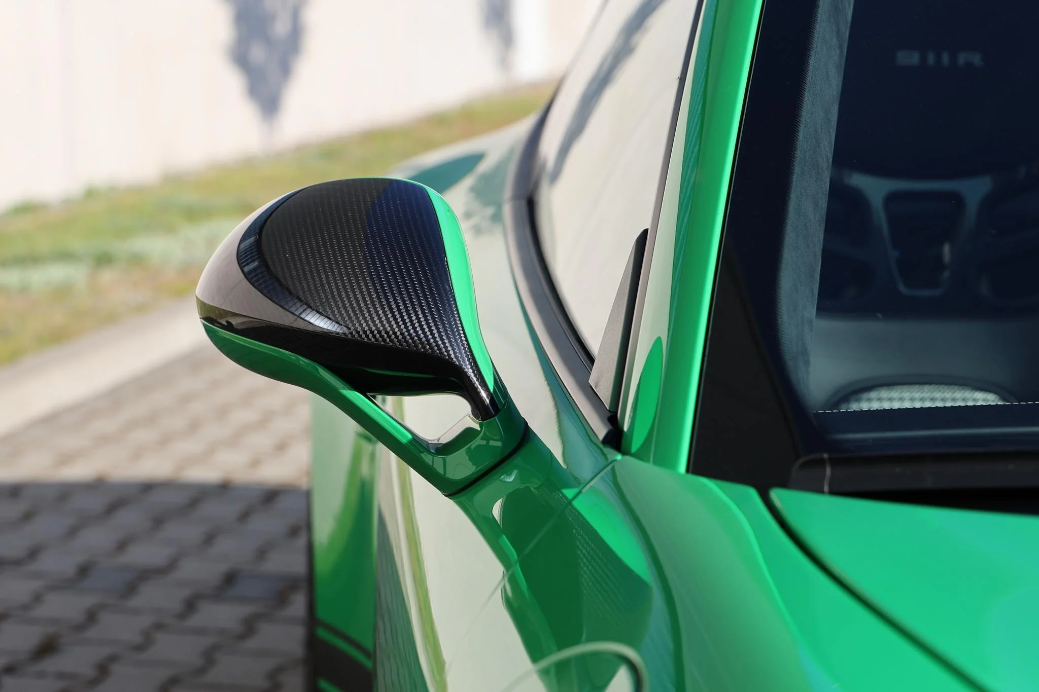 Left carbon fiber mirror cover of Viper Green Porsche 911R with white stripes on brick with concrete background for sale at FlowHaus