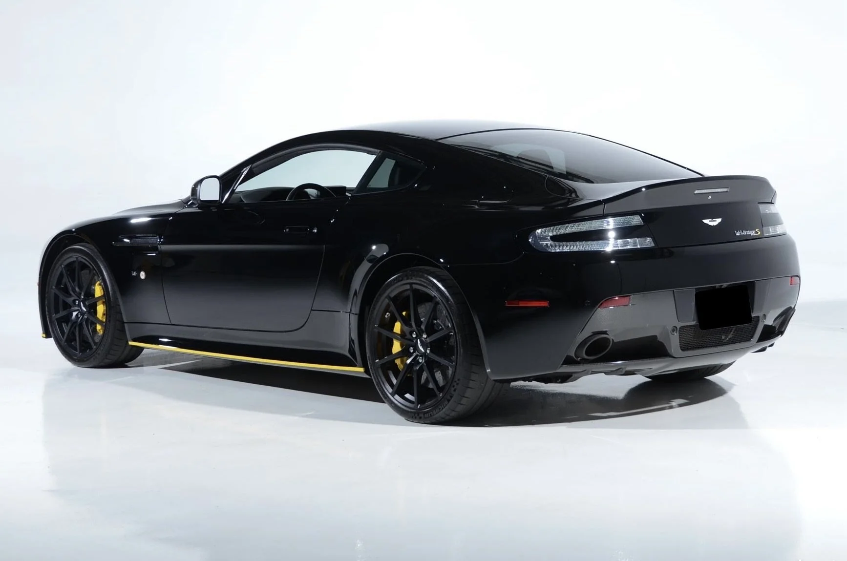 Black Aston Martin V8 Vantage S sports car with yellow brake calipers, parked on a plain white background.
