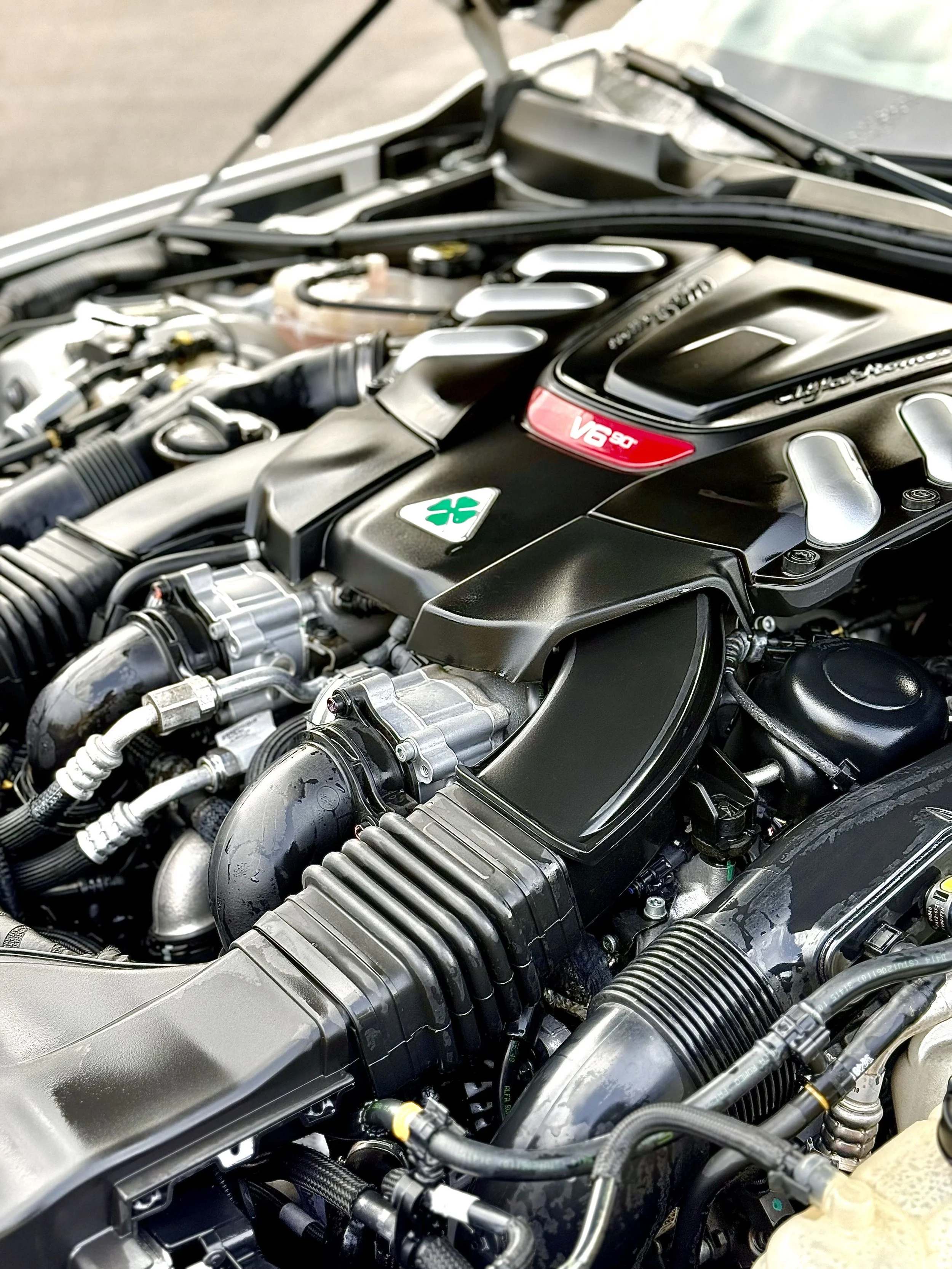 Close-up of a modern car engine with black plastic covers, metal components, and visible hoses and wires.