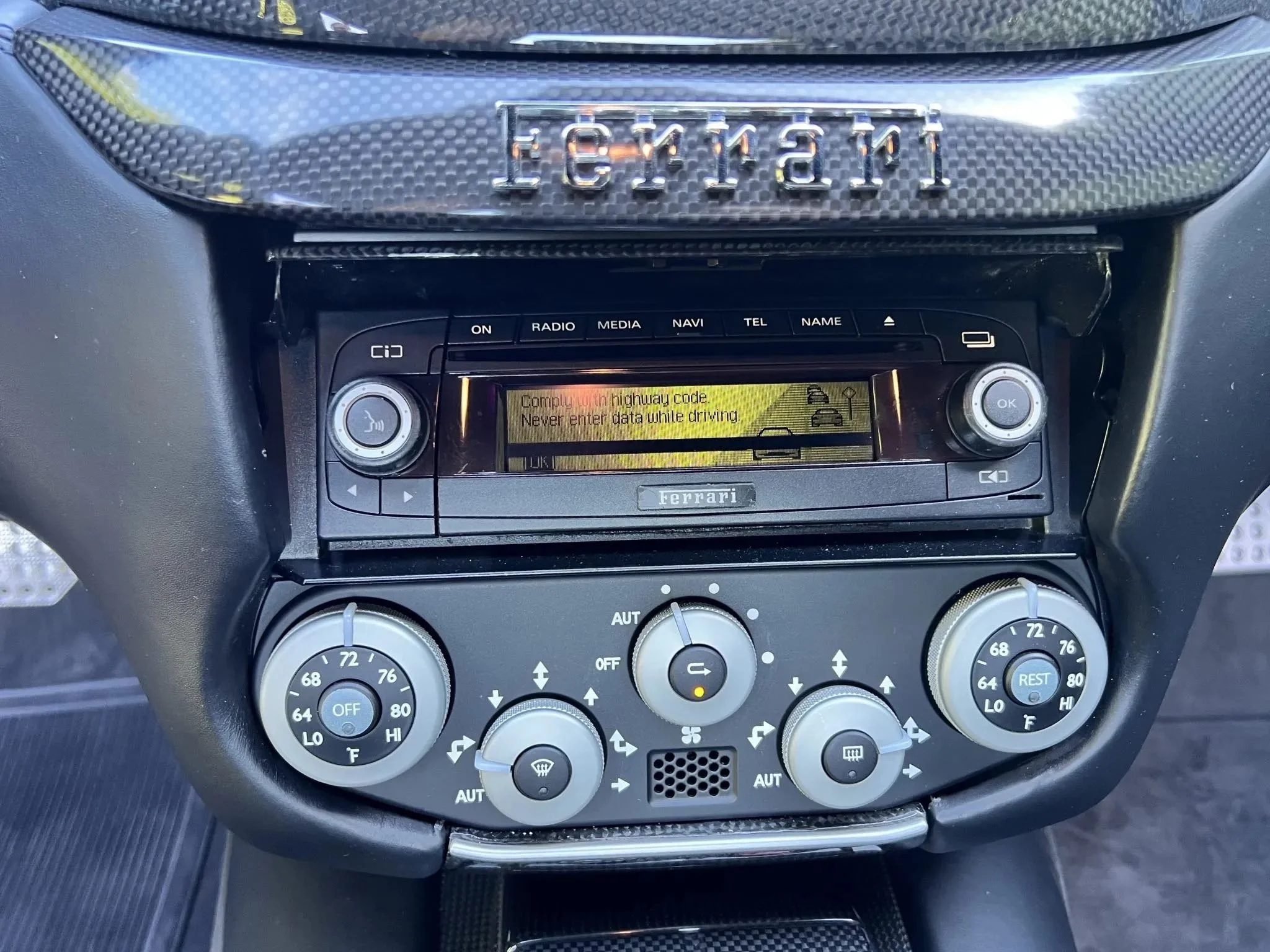 The interior dashboard of a Ferrari sports car, featuring climate control dials and a digital display screen.