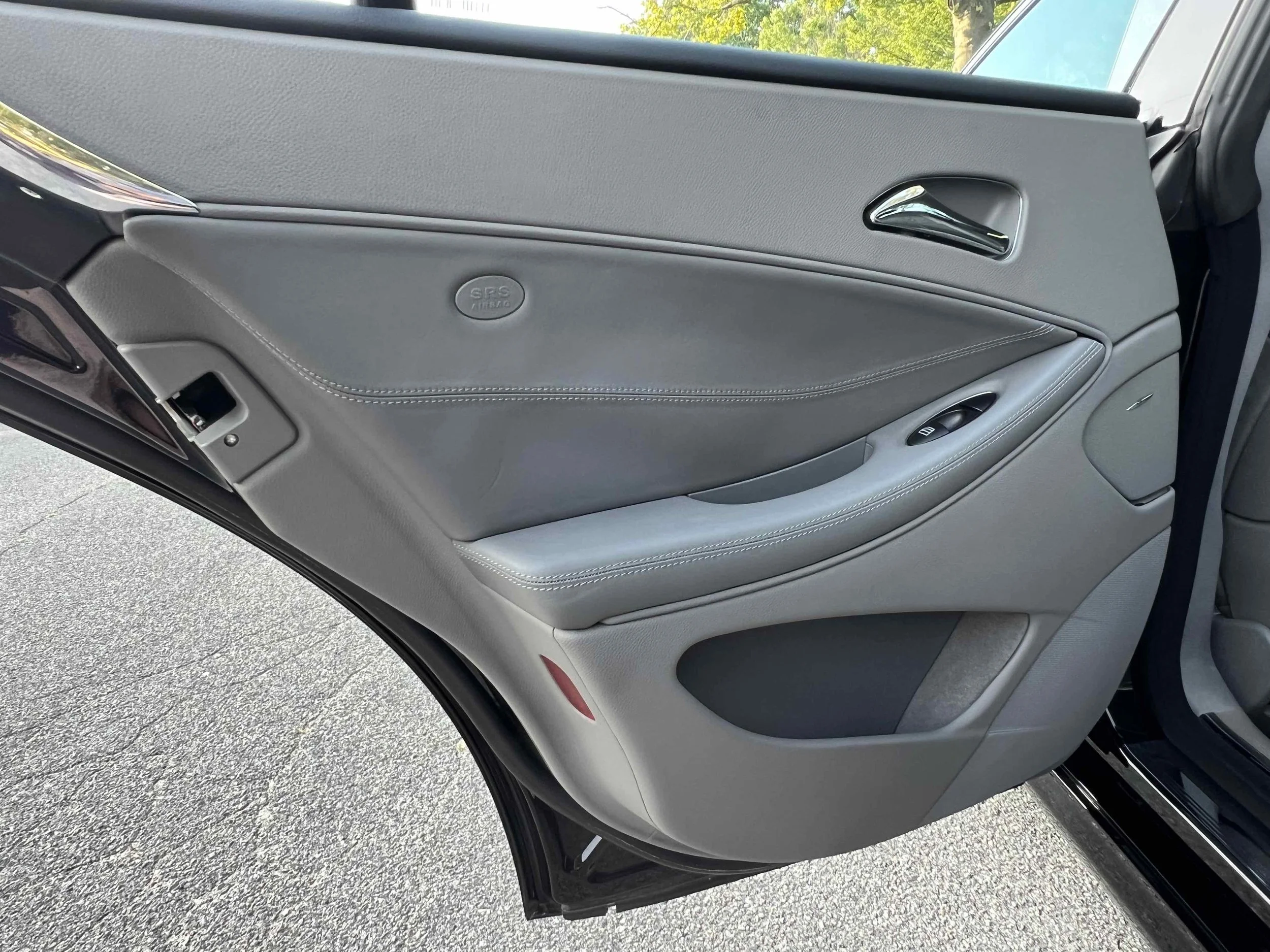 Inside view of a grey car door with a window control, door handle, and speaker.