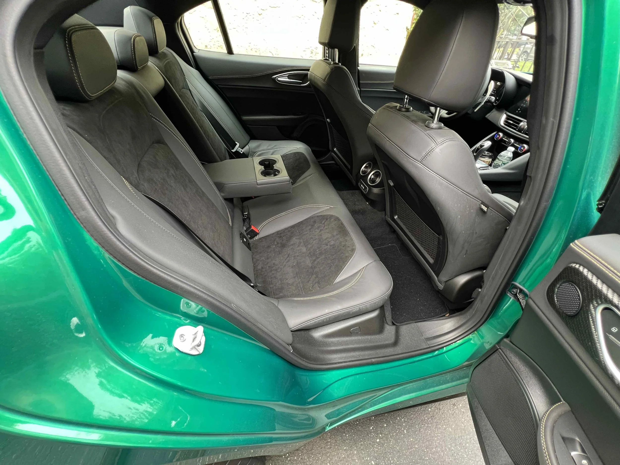 Interior of a modern green car showing the back seat with black leather seats and an armrest with cup holders, front seats, and dashboard.