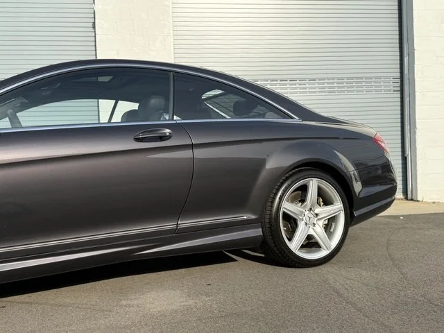 Driver side rear of Grey 2008 Mercedes Benz CL63 AMG on pavement with two green garage doors in the background for sale at FlowHaus