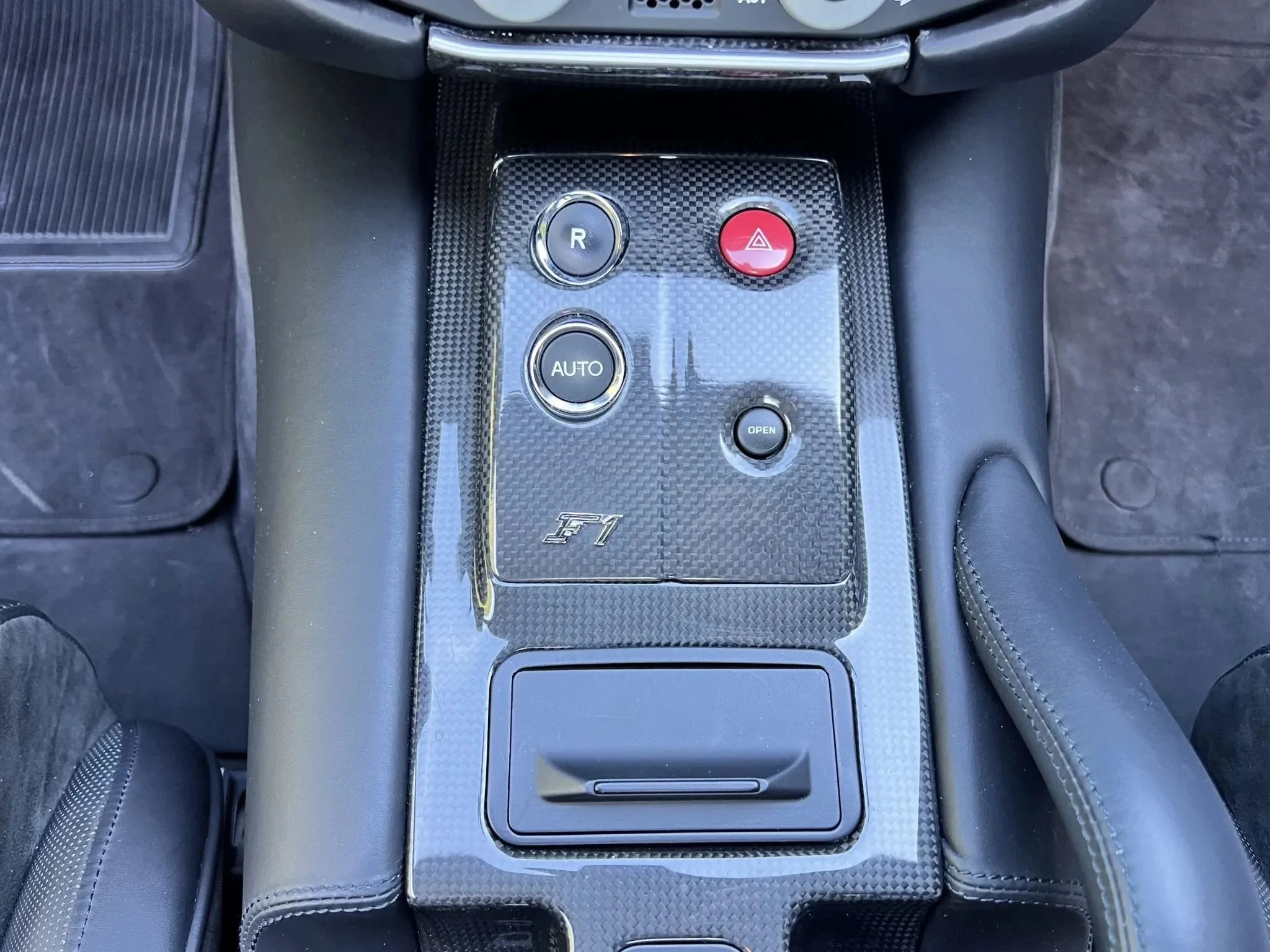 Center console of a car with carbon fiber finish featuring buttons labeled R, AUTO, open, and a red hazard warning button.