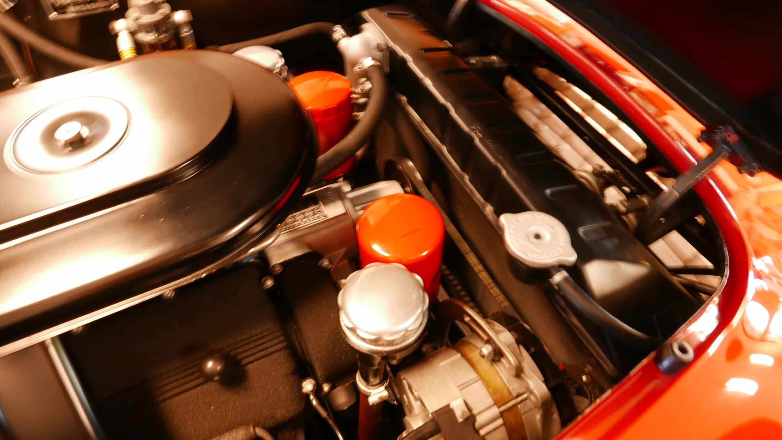 Close-up of a car engine bay showing an air filter, orange oil filter caps, a coolant reservoir, and various engine components.
