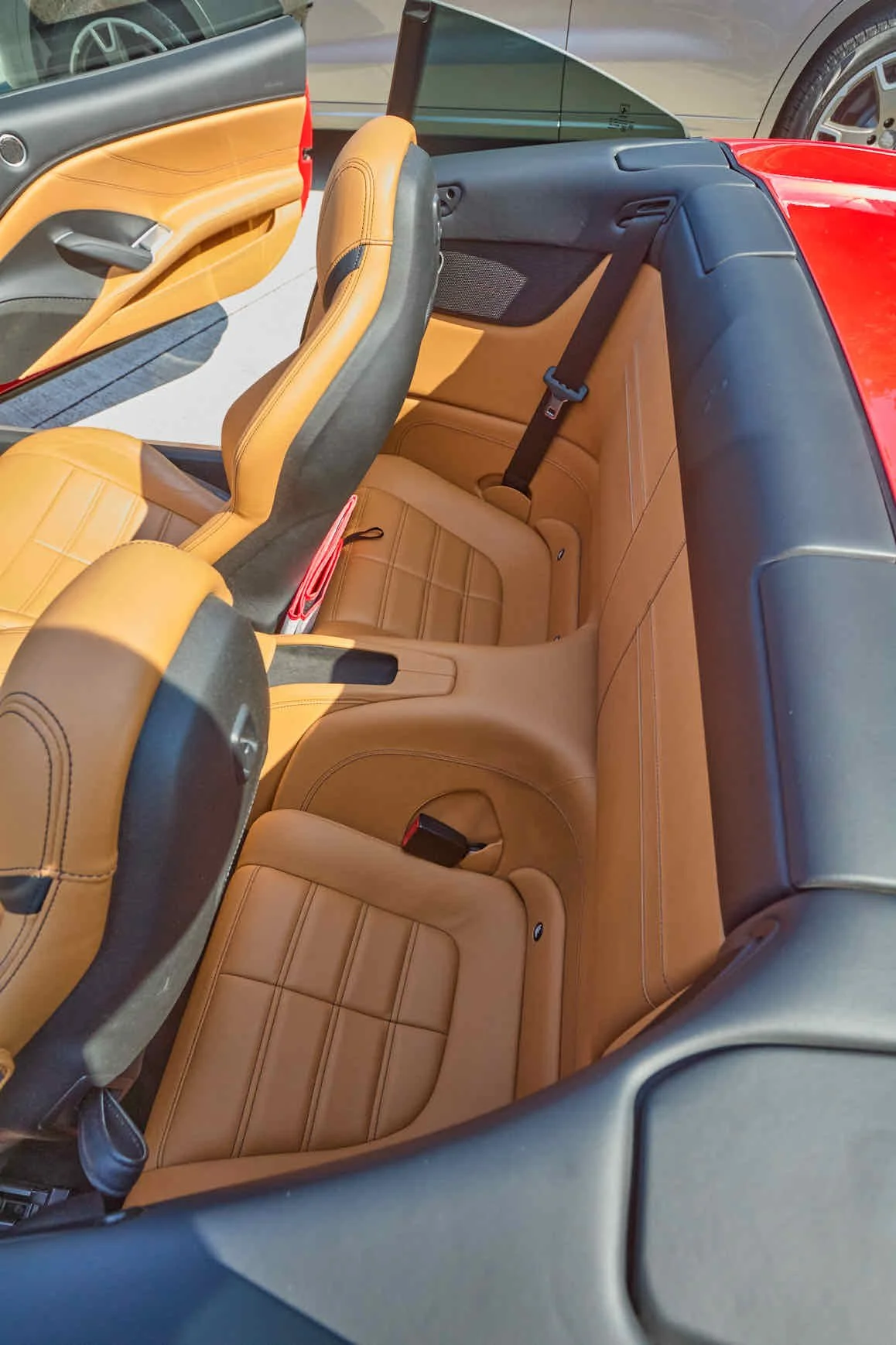 The interior of a red convertible sports car with tan leather seats, showing the back seats and part of the front seats.