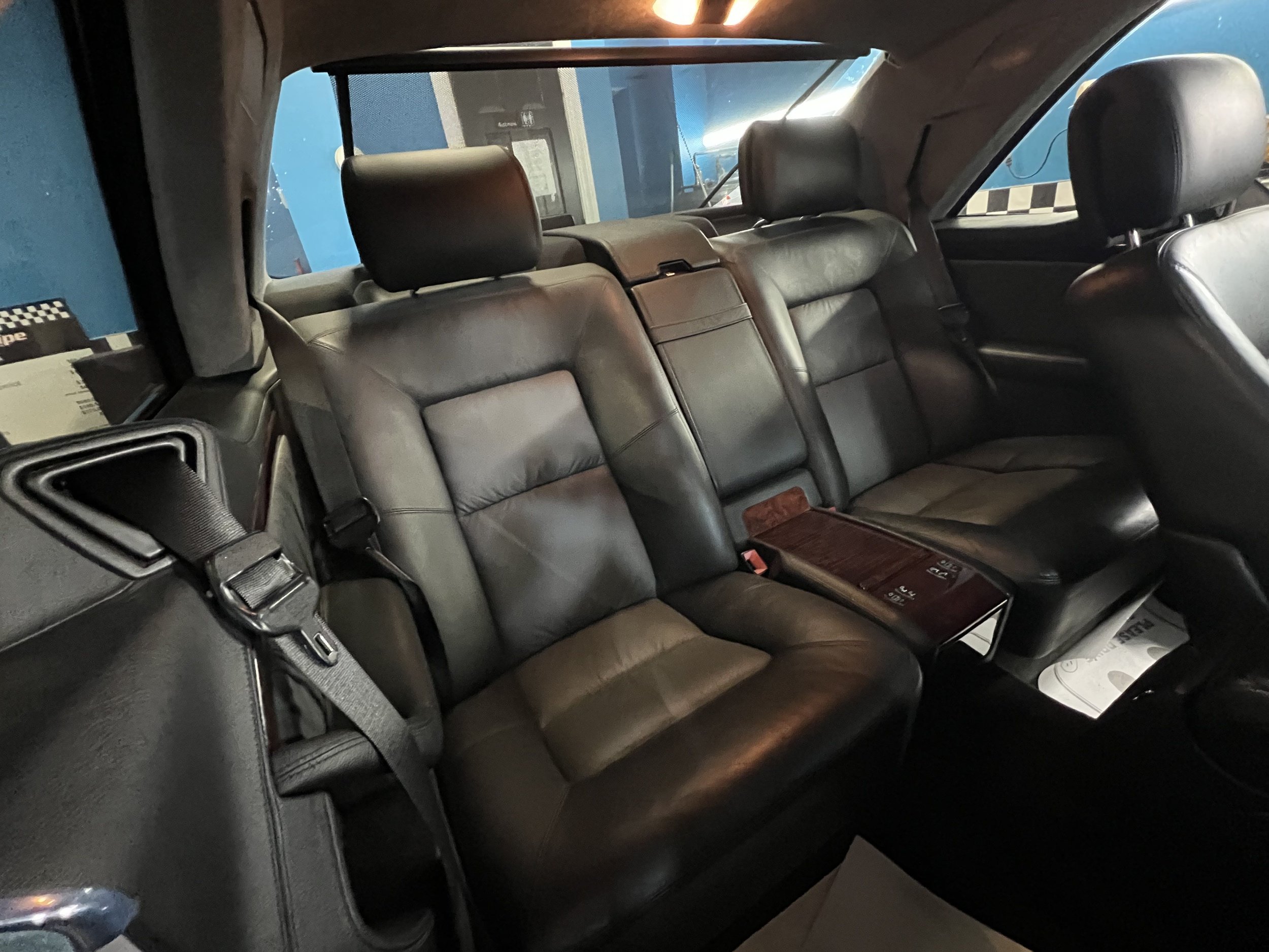 Interior of a car showing black leather backseat with three seats, headrests, seat belts, and a center console with controls.