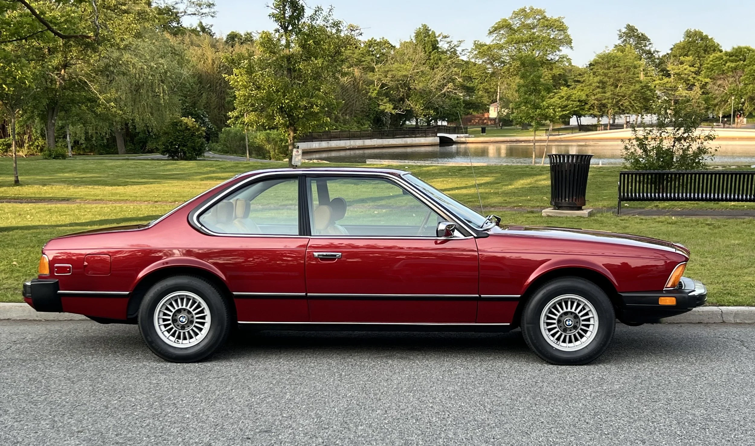 Side of Ruby Red 1977 BMW 630 csi on display in park for sale at FlowHaus