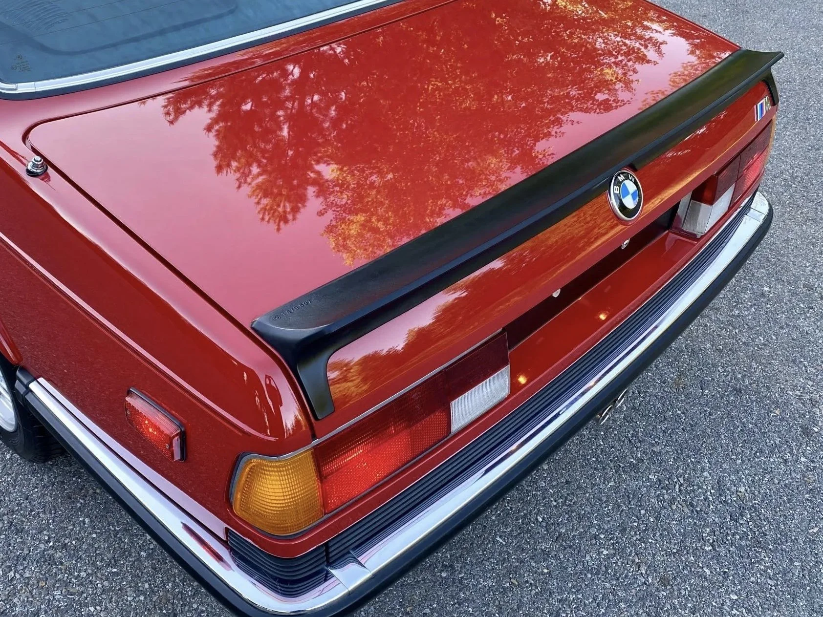 Rear view of a red vintage BMW car, showing the trunk, taillights, a black spoiler, and the BMW logo.