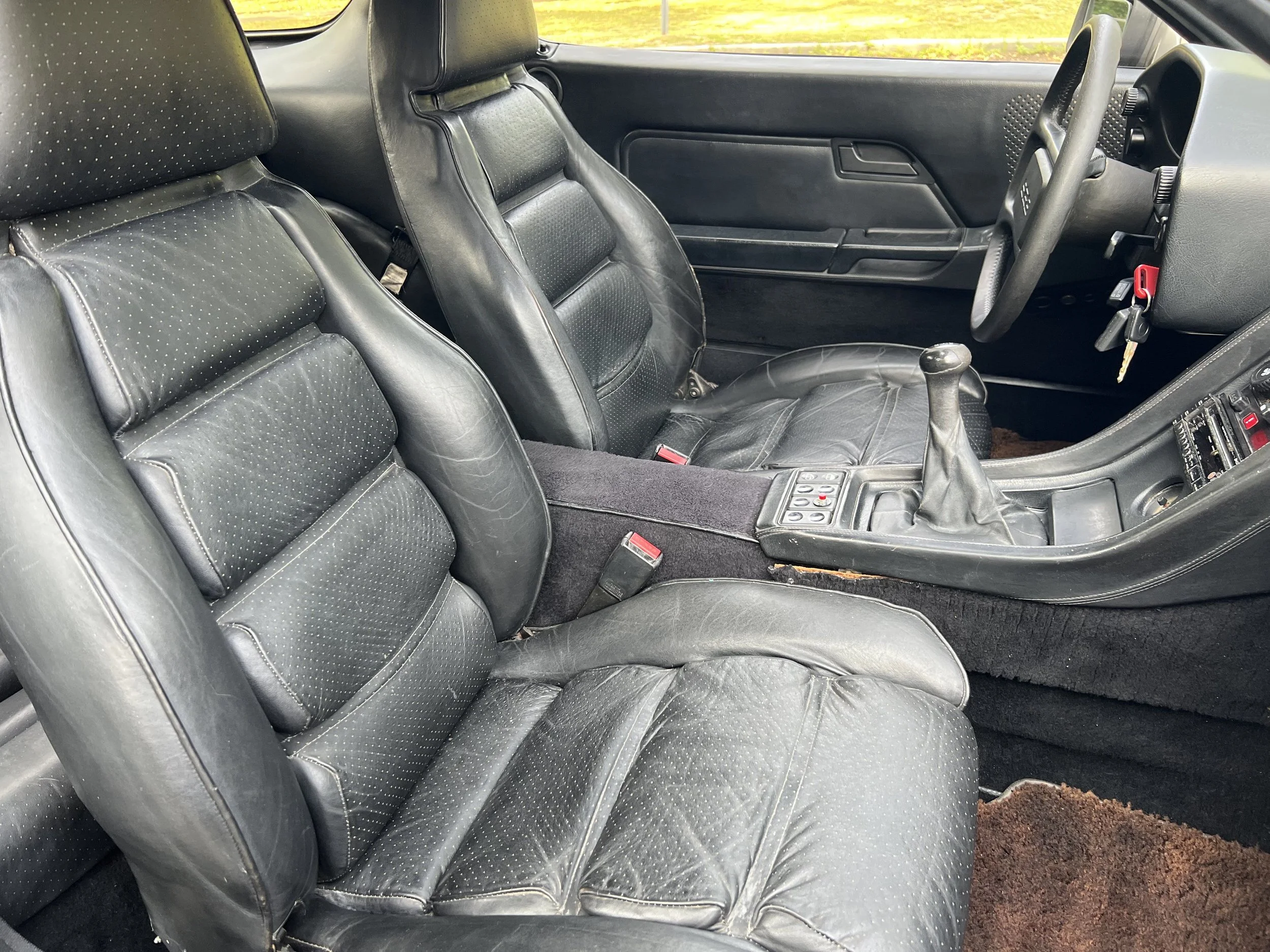 Interior of a car showing two black leather seats, a steering wheel, gear shift, and dashboard.