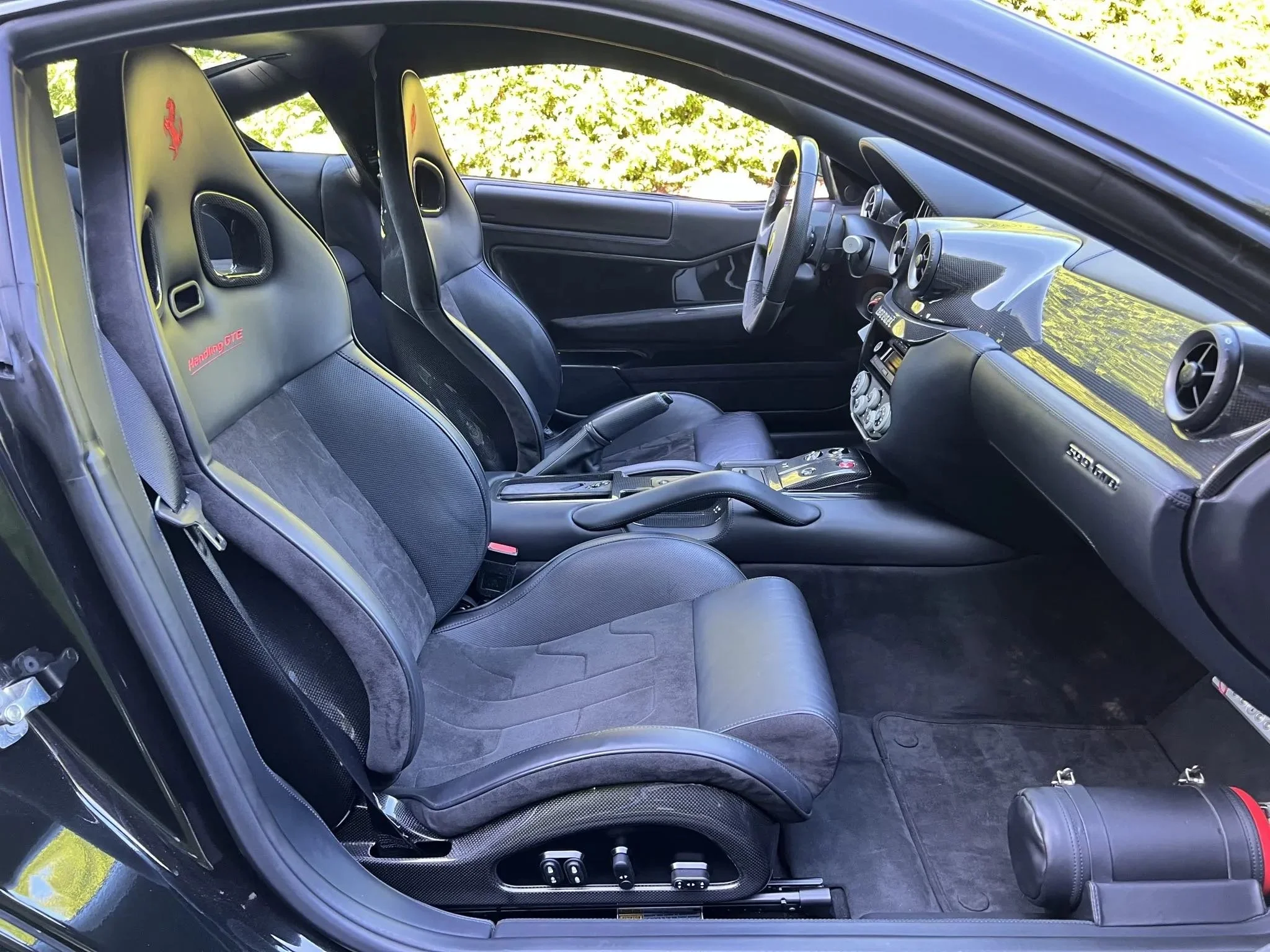 Interior of a black sports car with racing seats, a carbon fiber dashboard, and a manual transmission, parked outdoors.