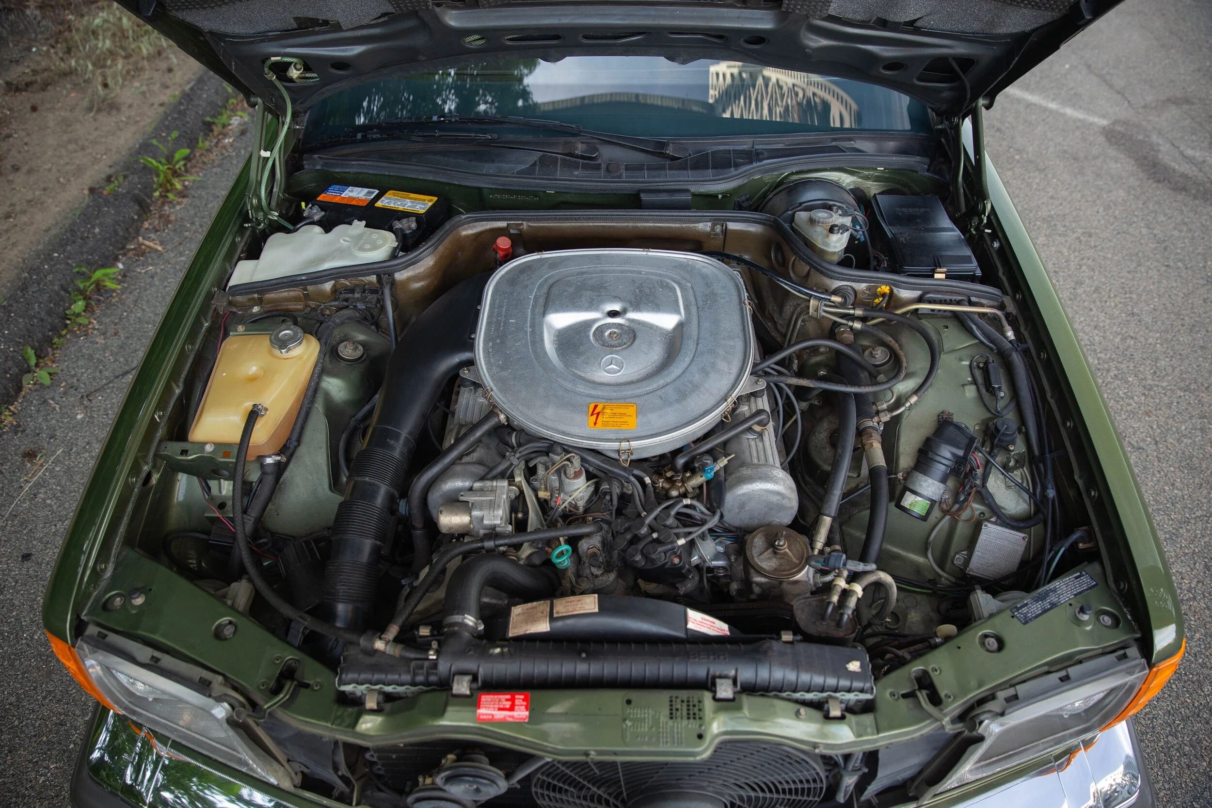 Engine bay of a classic Mercedes-Benz car with the hood open, showing engine parts, hoses, and components.