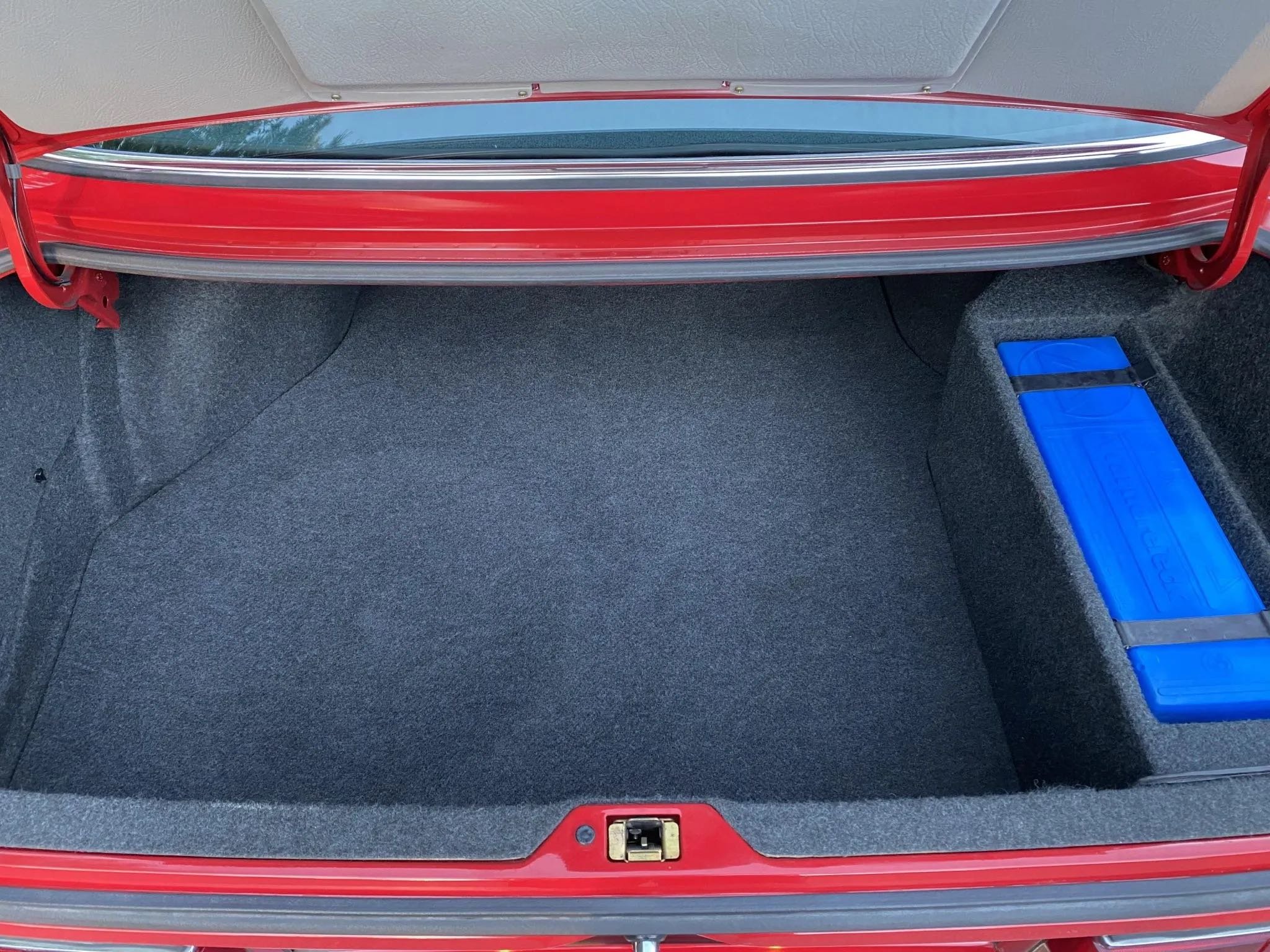 Open car trunk with a red exterior, gray carpeting, and a blue rectangular object secured inside on the right.