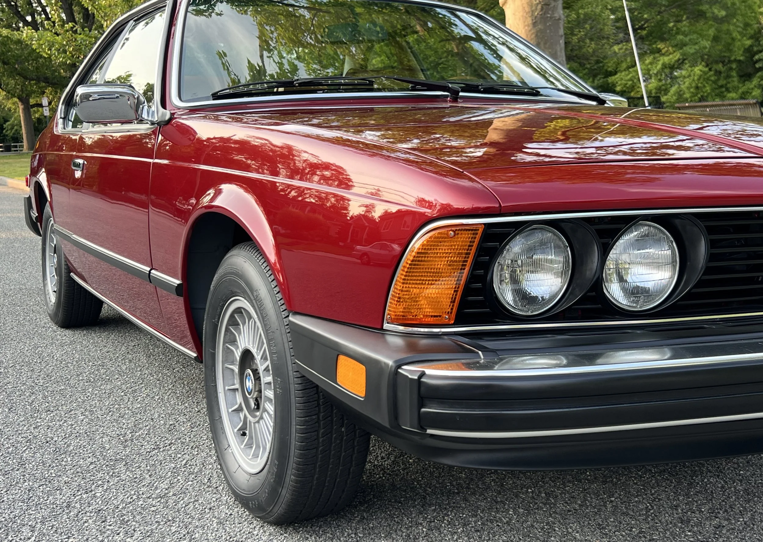 Red vintage BMW 630 CSI car parked on the street with trees in the background.