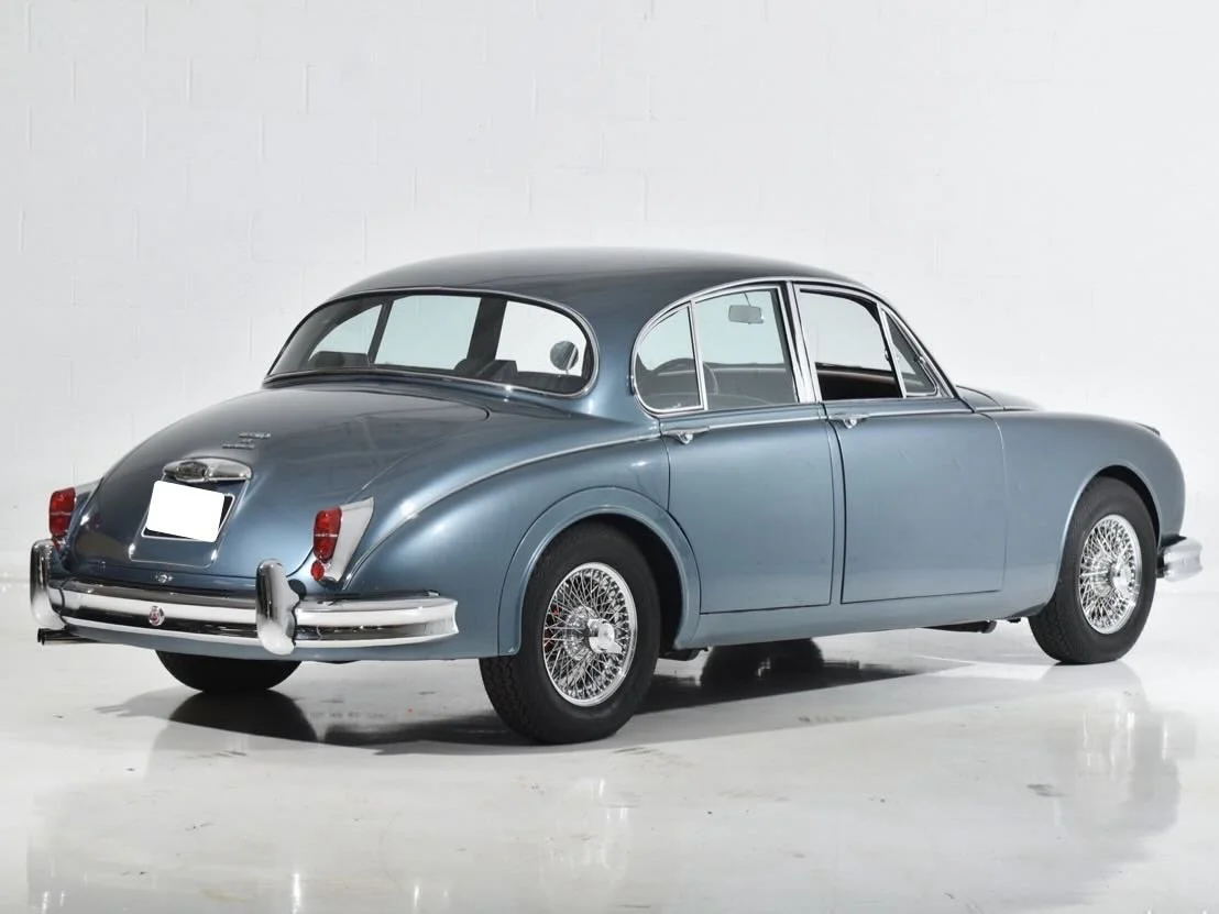A vintage blue classic car with wire-spoke wheels parked in a white studio.