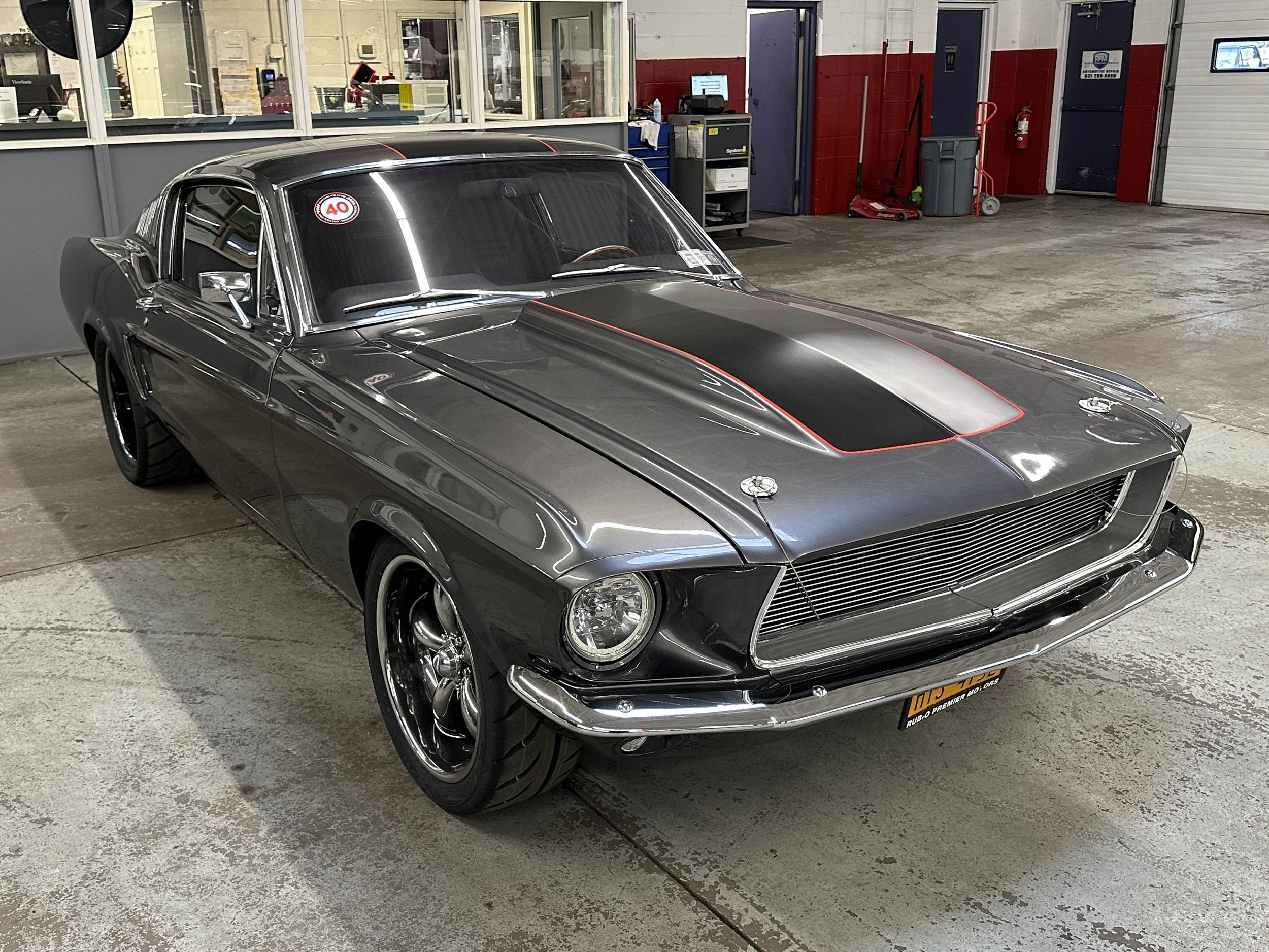 A vintage black muscle car with a sleek design, hood scoop, and red striping, parked inside a garage or workshop.