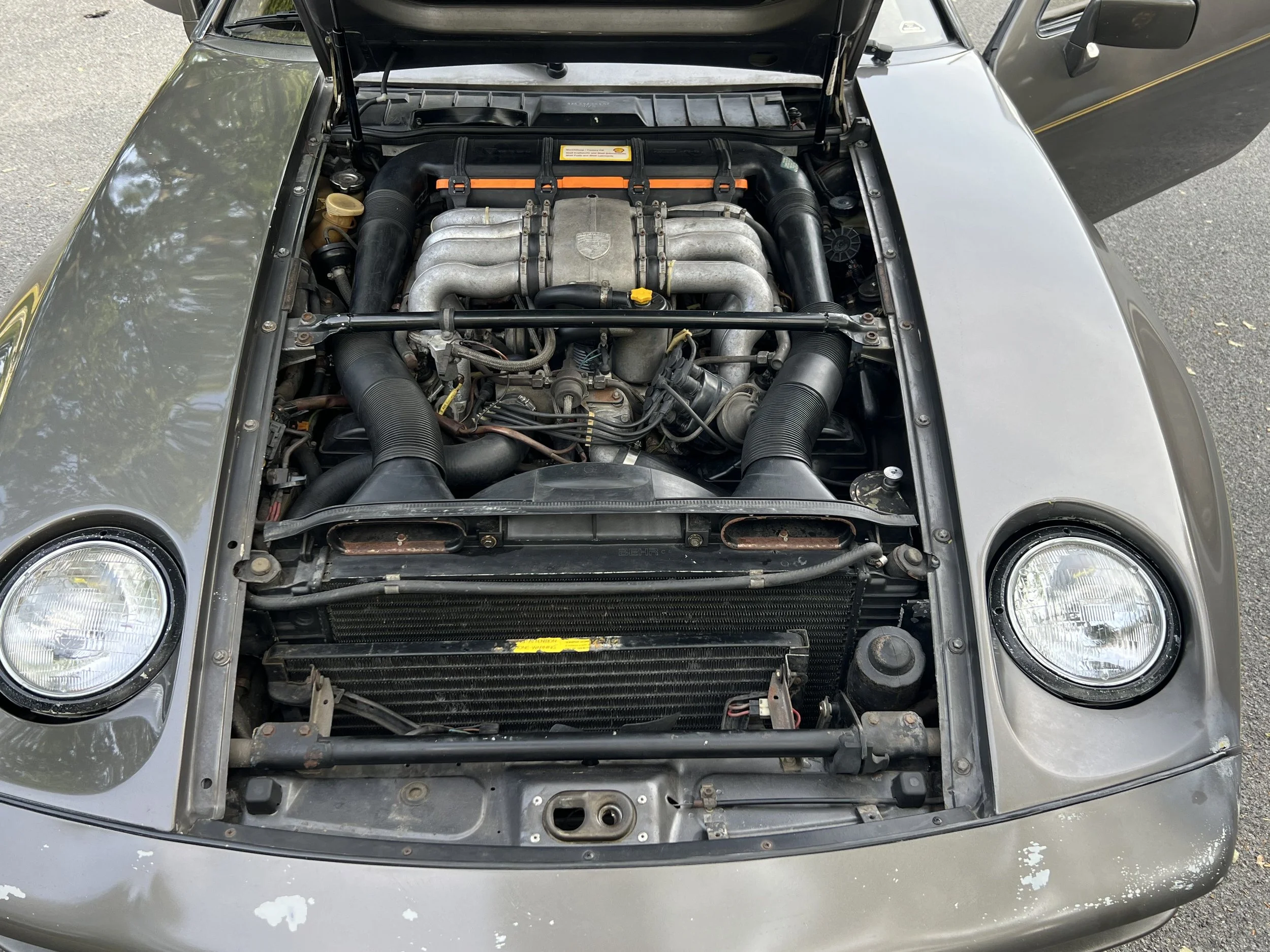 Front of a gray sports car with the hood open, revealing the engine, cooling radiator, and headlamps.