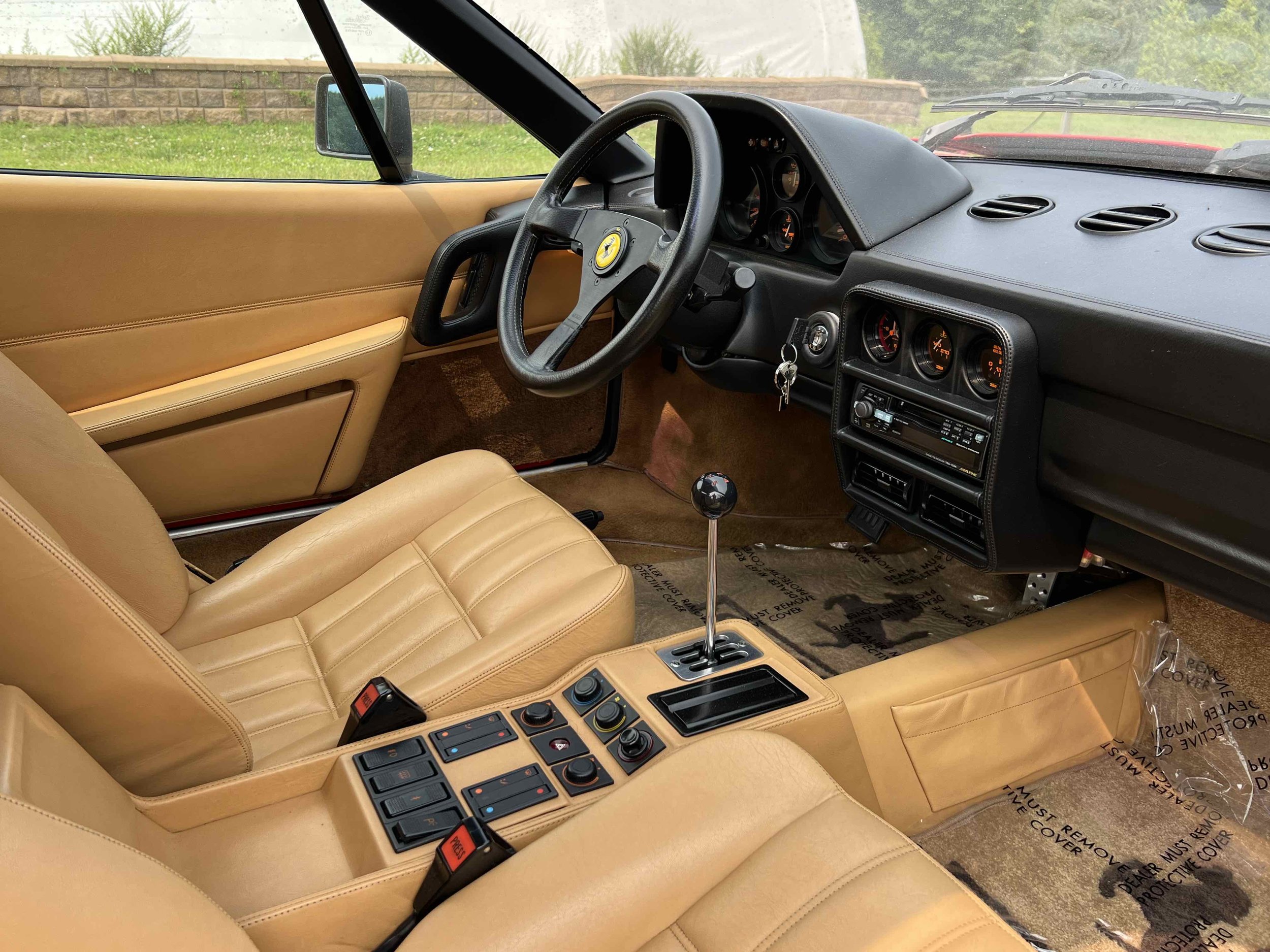 Interior of a vintage sports car with tan leather seats, black dashboard, and race-inspired controls, featuring a manual gear shifter.