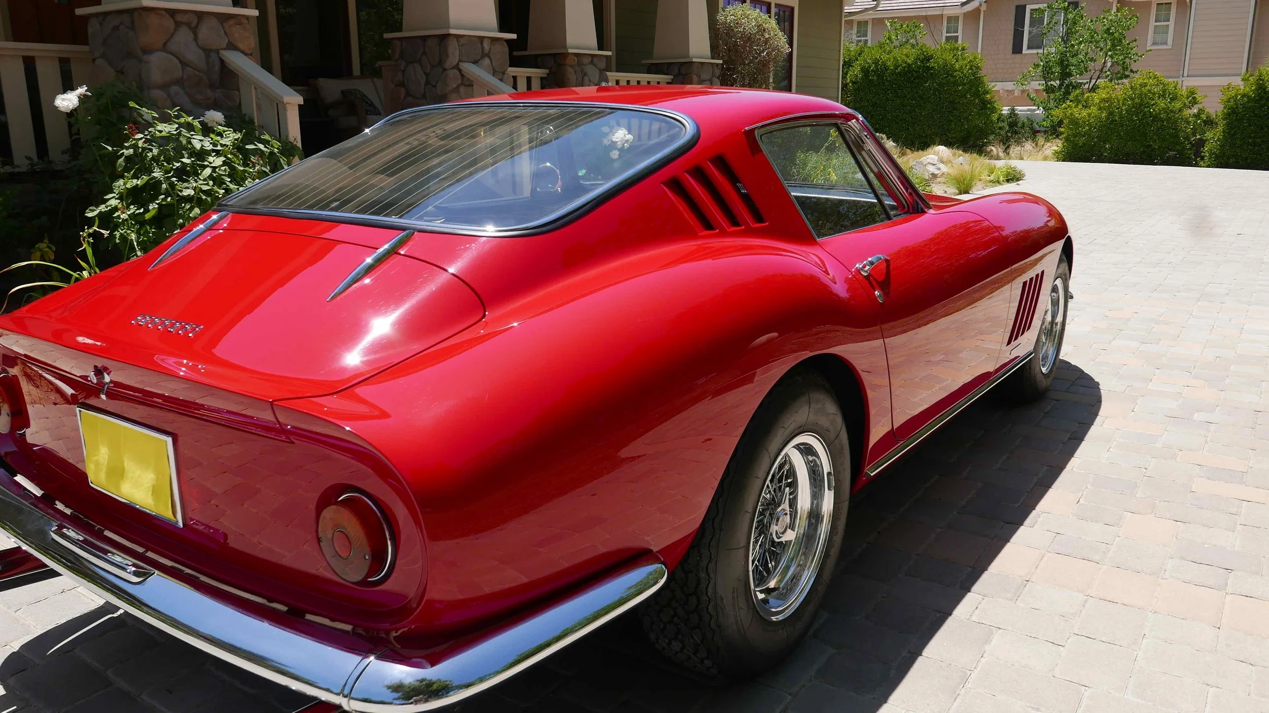 Red vintage Ferrari sports car parked on a brick driveway, with a residential background and greenery.