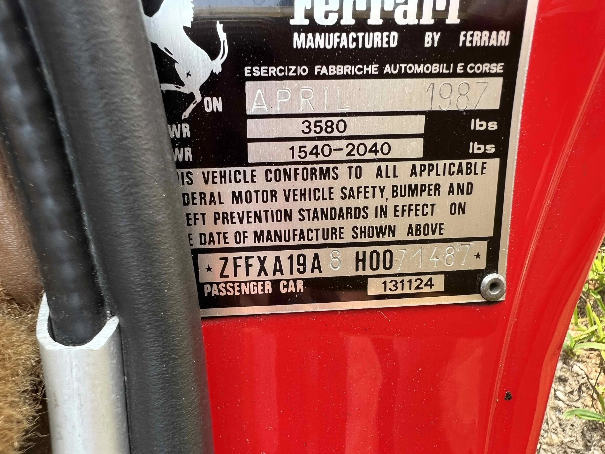Vehicle identification and safety information plate on a red Ferrari, showing manufacturing details, model, and weight specifications.