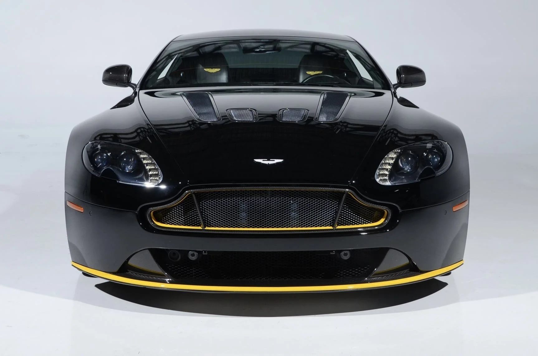 Front view of a black luxury sports car with yellow accents, carbon fiber details, and a sleek aerodynamic design, displayed in a white studio setting.
