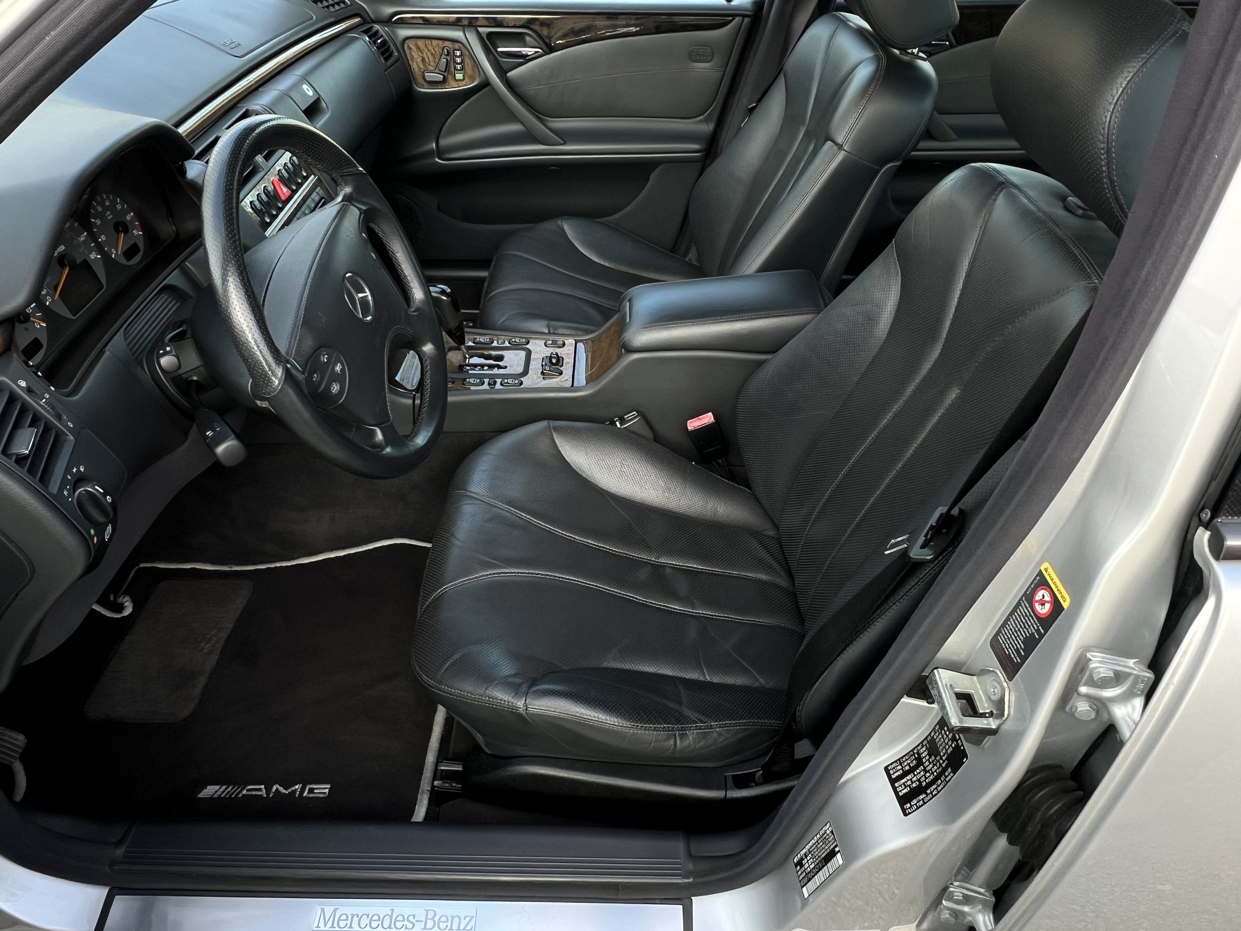 Interior of a luxury Mercedes-Benz vehicle with black leather seats, wood trim, and a dashboard with various controls.