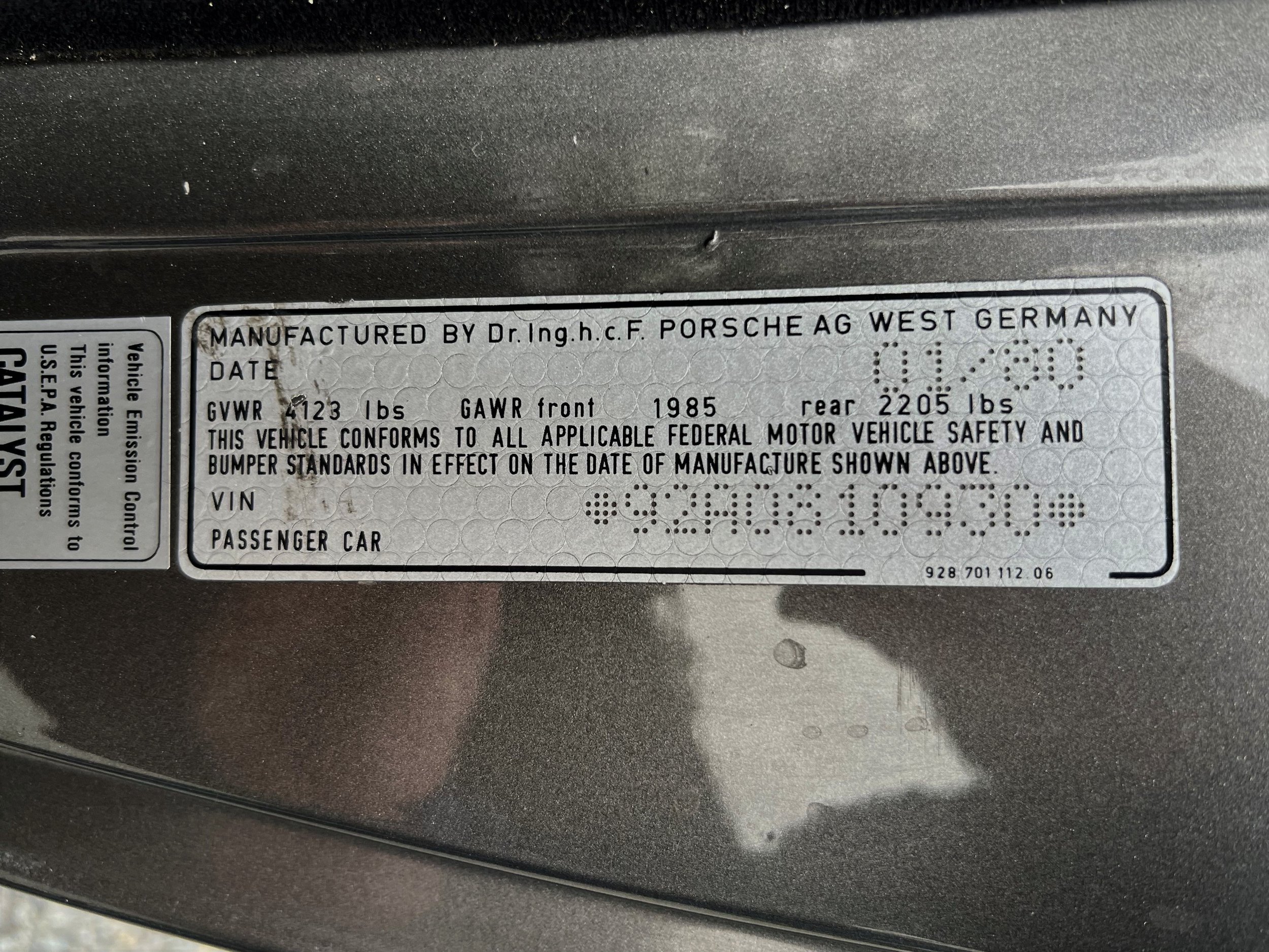 Vehicle information label on a Porsche car indicating manufacturing details, weight limits, and compliance with federal safety standards.