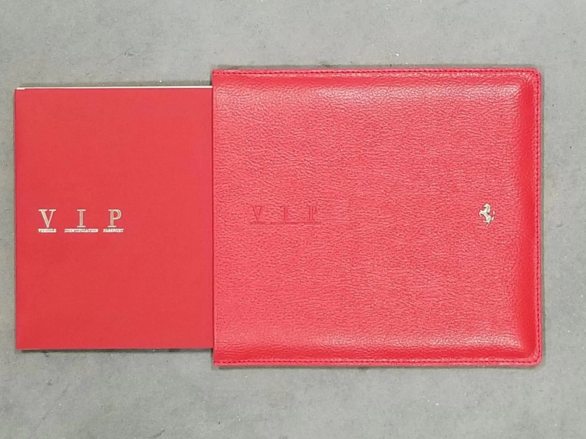 A red folder with the Ferrari logo and a red VIP booklet placed on a gray surface.