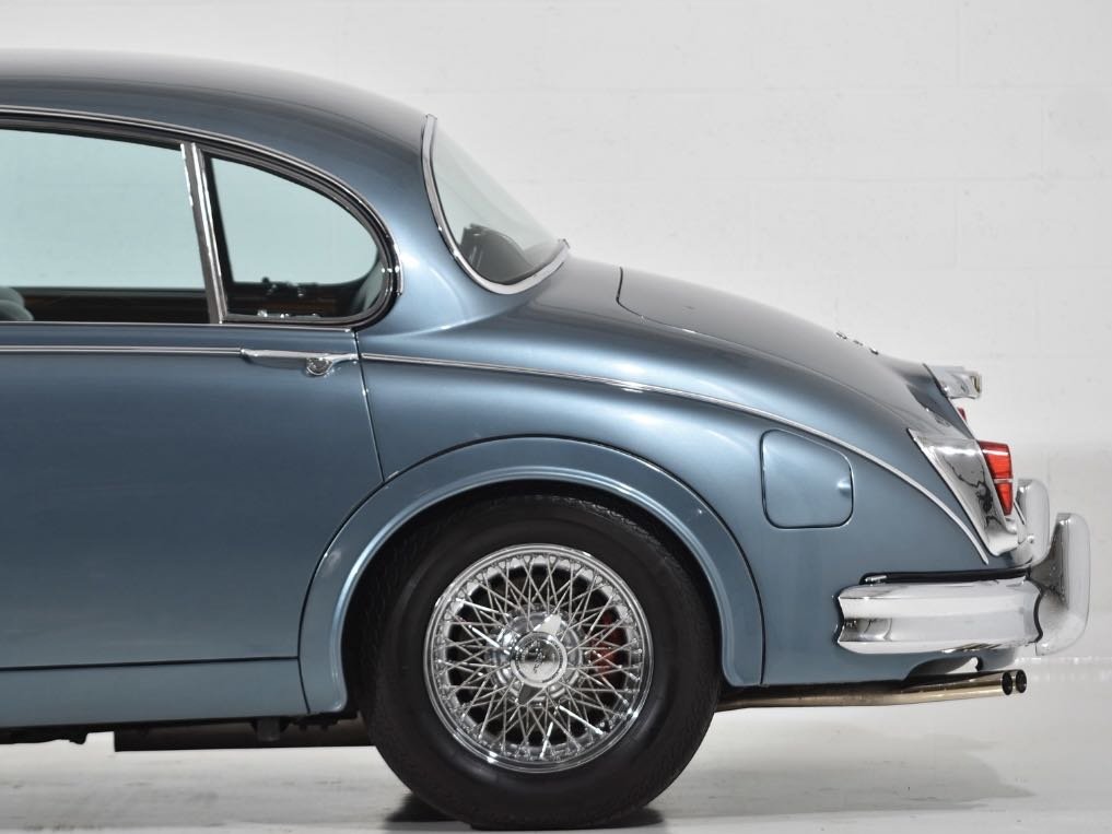 Close-up of a vintage light blue car showing the side, wheel with wire spokes, and part of the rear bumper.