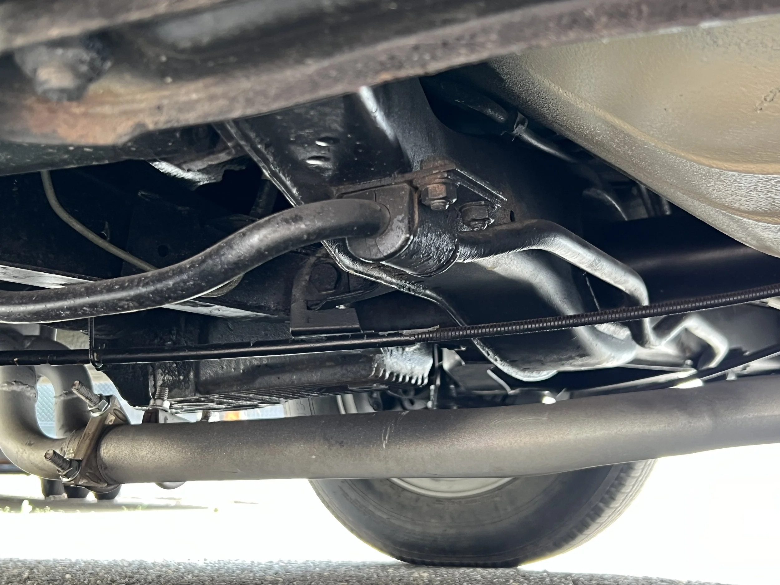 Underneath view of a 1977 BMW 630 csi vehicle showing part of the frame, oil pan, and various drivetrain components.