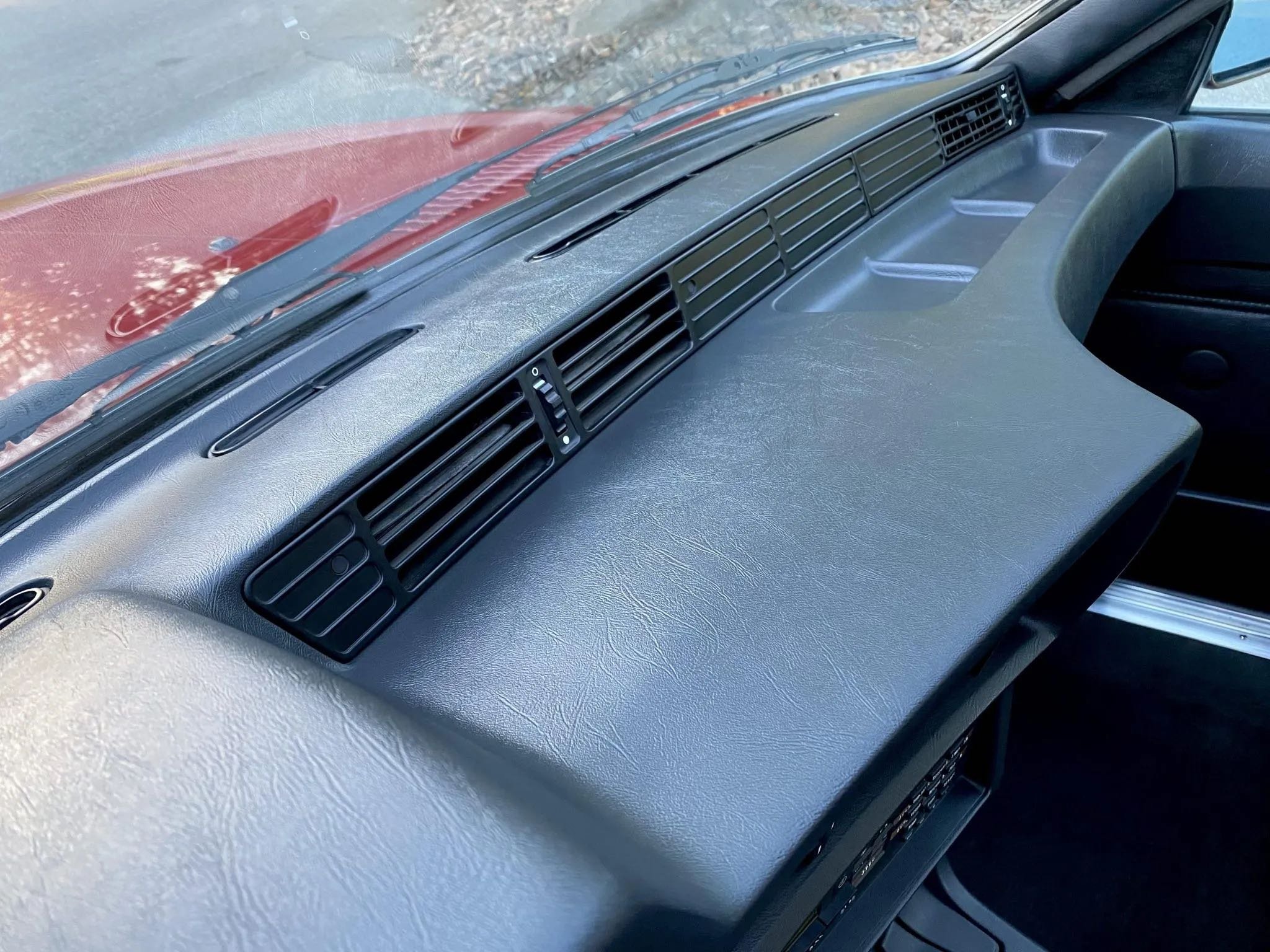 Close-up of a vehicle dashboard with several air vents and a textured surface, looking from the passenger side.