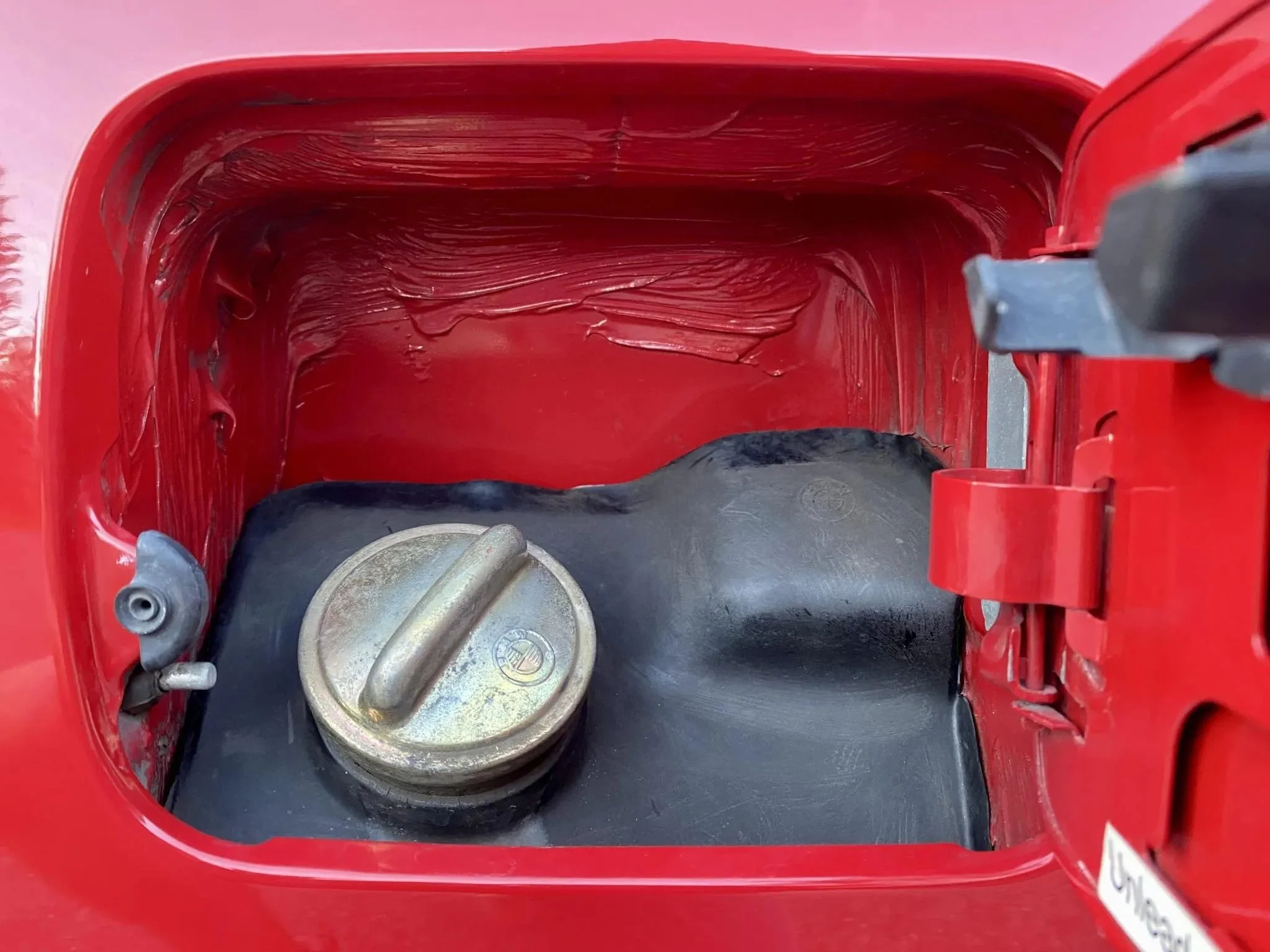 Inside of a red gasoline container with a black rubber seal and a metal cap.