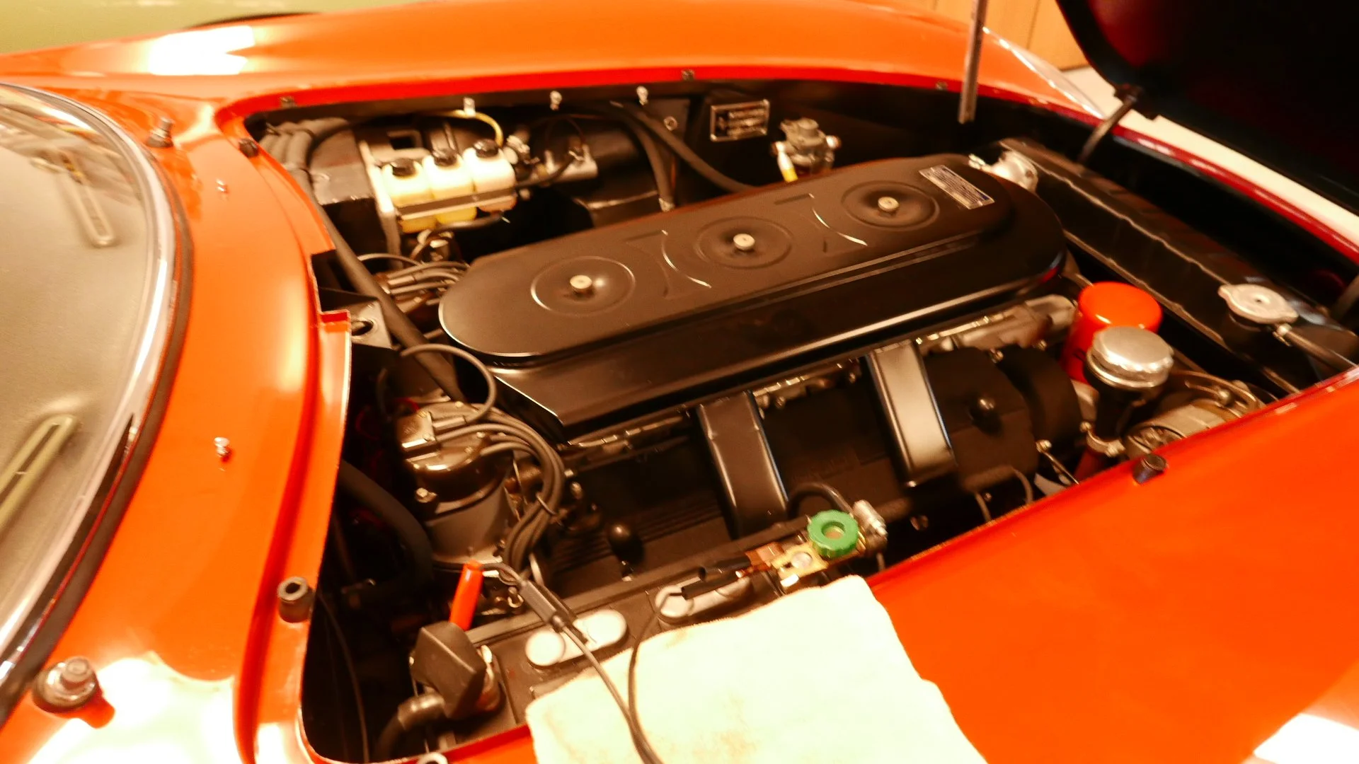 Engine of a classic orange car with detailed mechanical parts visible under the open hood.