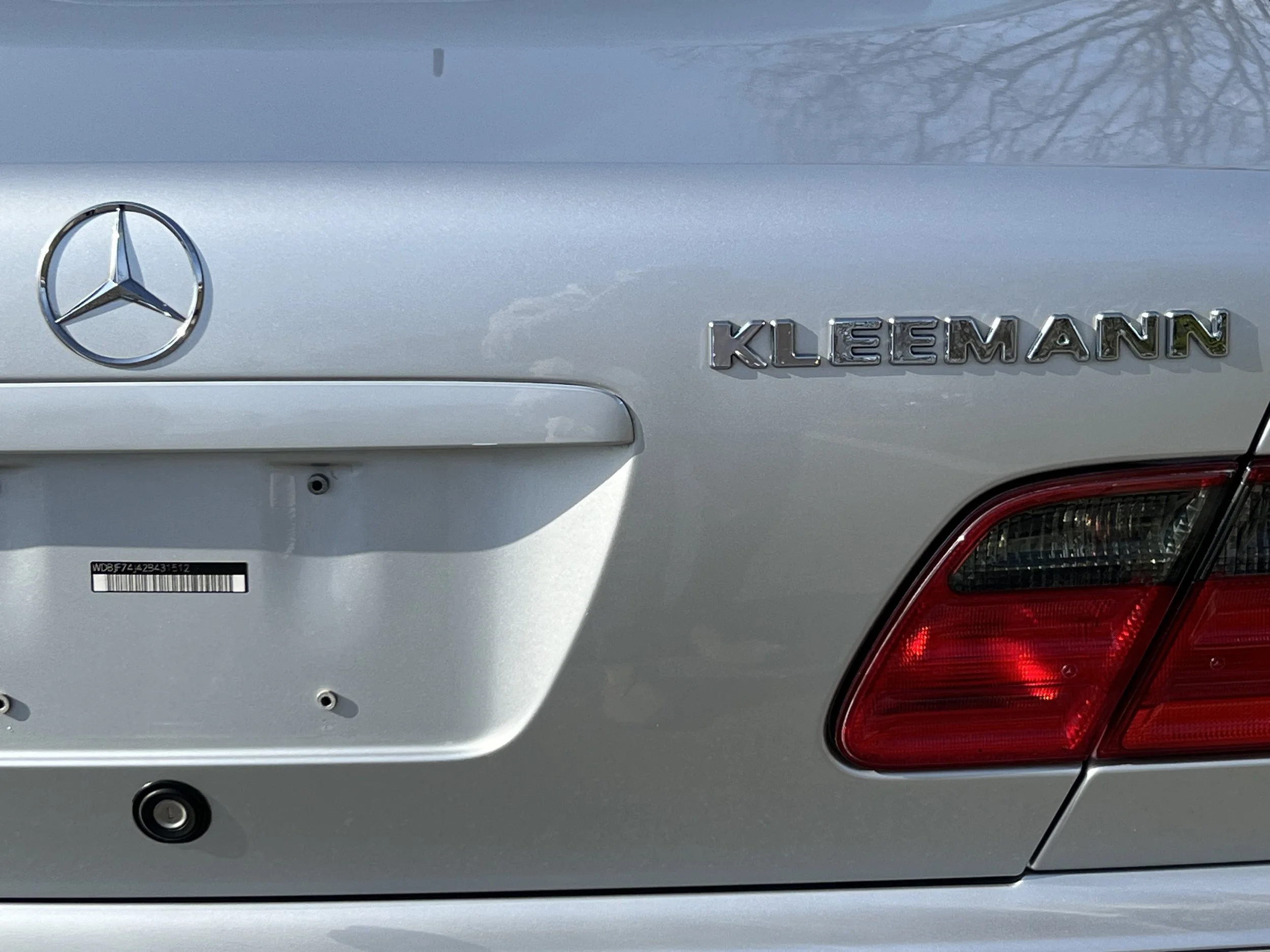Close-up of the rear of a silver Mercedes-Benz car with the model name Klee Mann, taillight, and part of the trunk door visible.