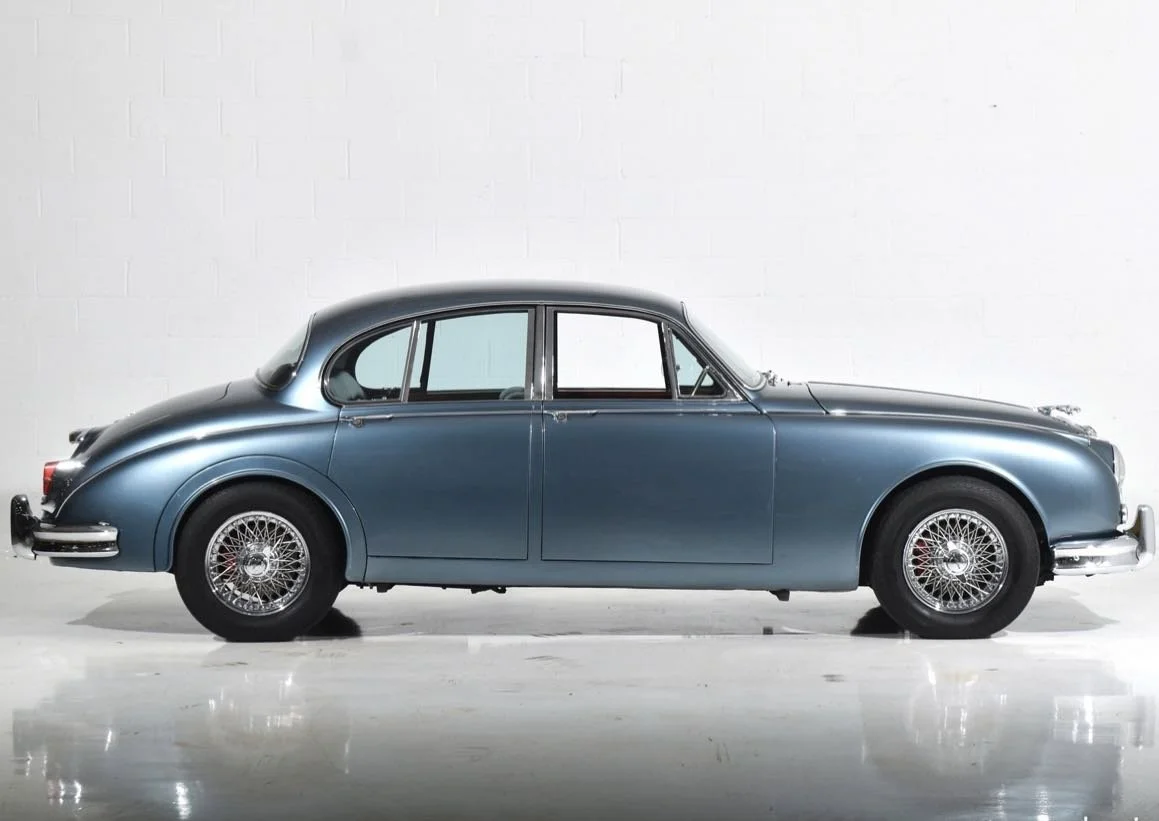 A classic vintage blue sedan car parked indoors against a plain white wall.
