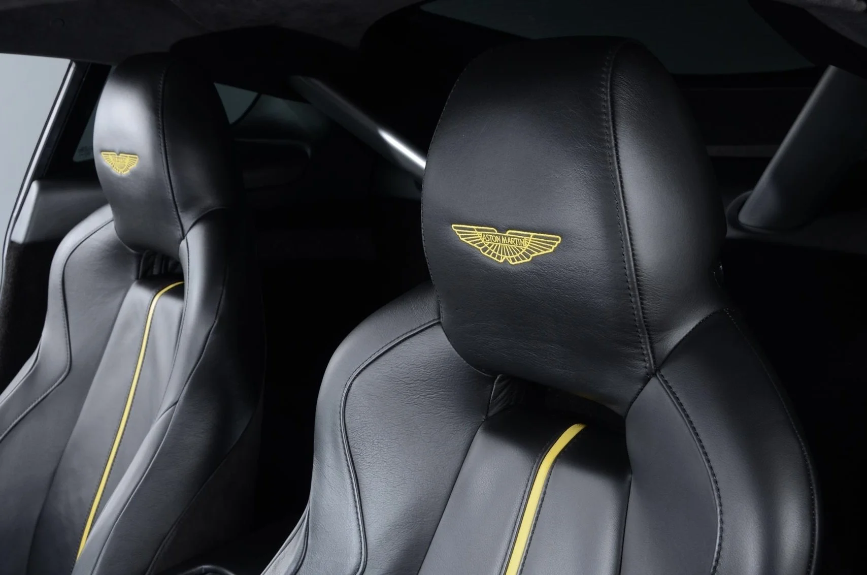 Close-up of black leather car seats with yellow stitching and the Aston Martin logo embroidered on the headrests.