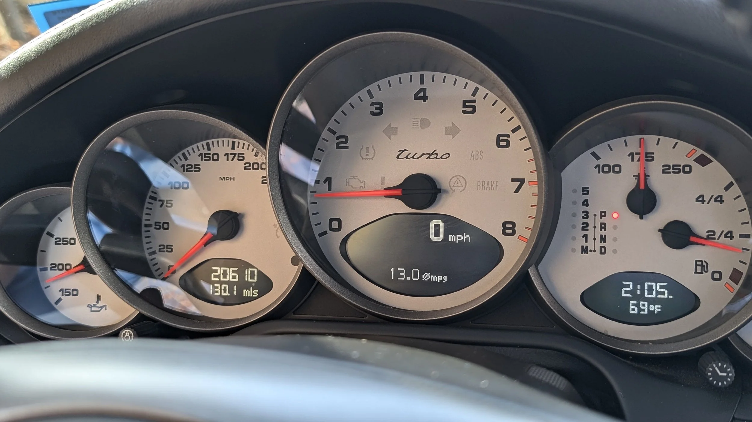 Close-up view of a car dashboard showing the speedometer at 0 mph, tachometer at 1,000 rpm, fuel gauge at two-thirds full, and digital displays indicating 2:05 PM, 69°F, 20610 miles driven, and 13.0 mpg.