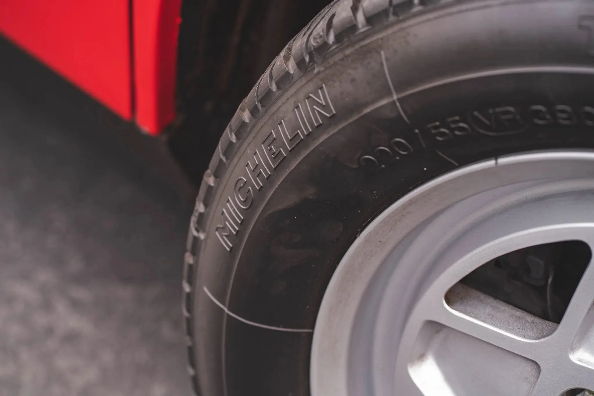 Close-up of a Michelin tire mounted on a vehicle, with part of the red vehicle body visible in the background.