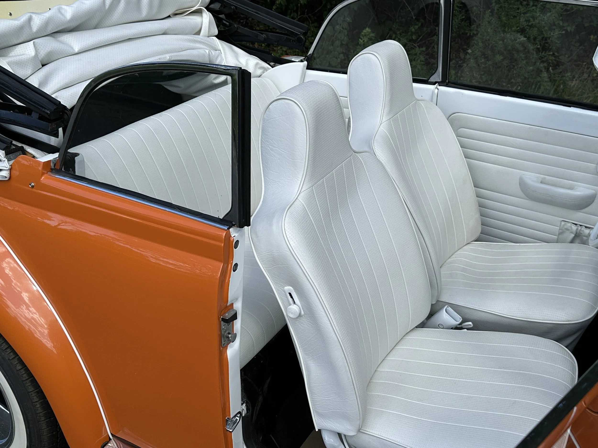 Interior of a vintage orange convertible car showing white vinyl seats and black-framed windshield.