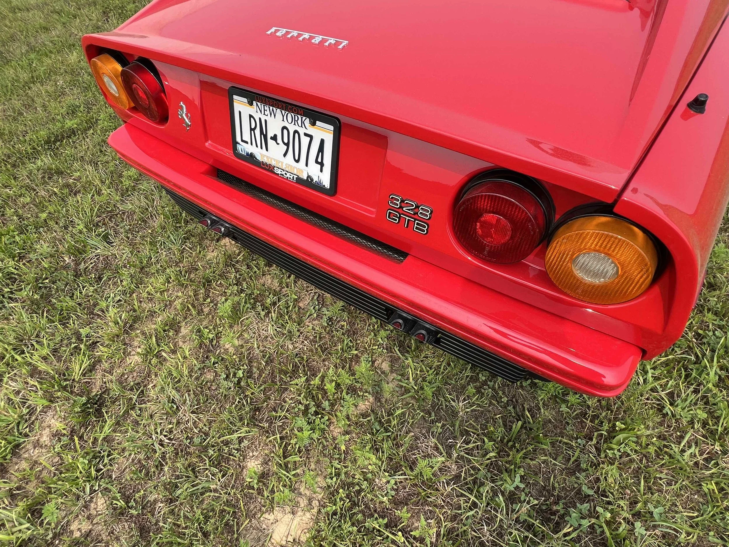 Red Ferrari sports car showing its rear, including tail lights, license plate, and emblem, positioned on grass.