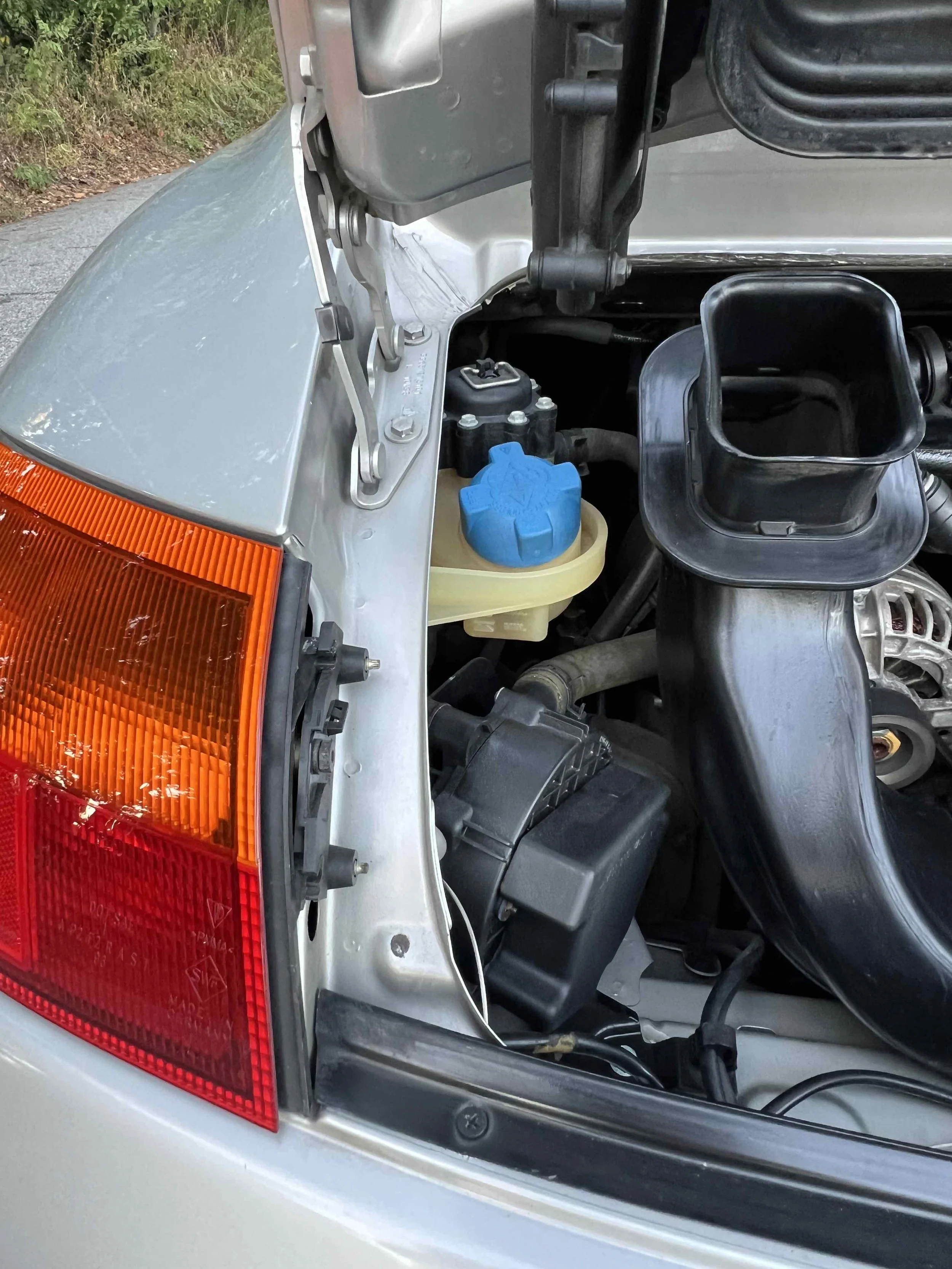 Close-up of a car's engine bay showing the headlight, engine components, and a blue windshield washer fluid cap.