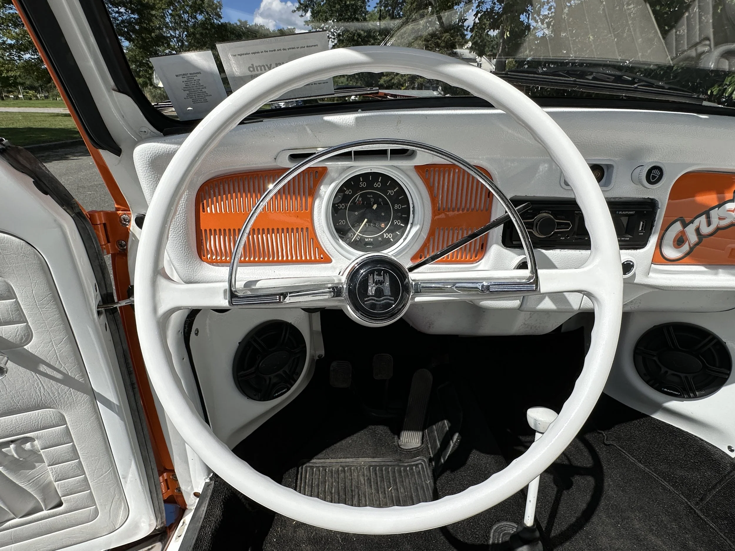 Interior of a vintage Volkswagen Beetle showing the dashboard, steering wheel, and speedometer, with orange accents and black speakers.