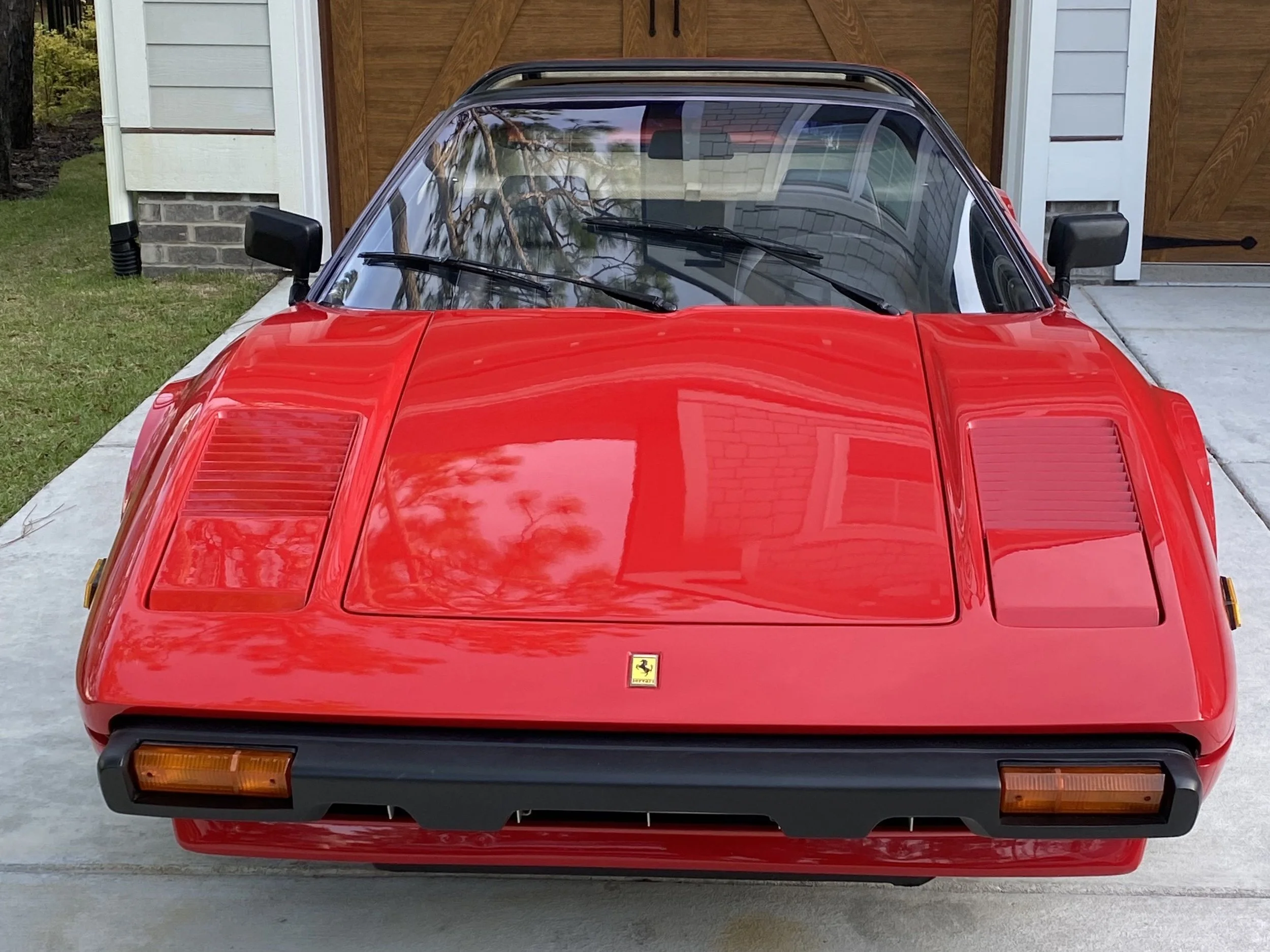 Front view of a red vintage Ferrari sports car parked on a driveway, with a garage door in the background.