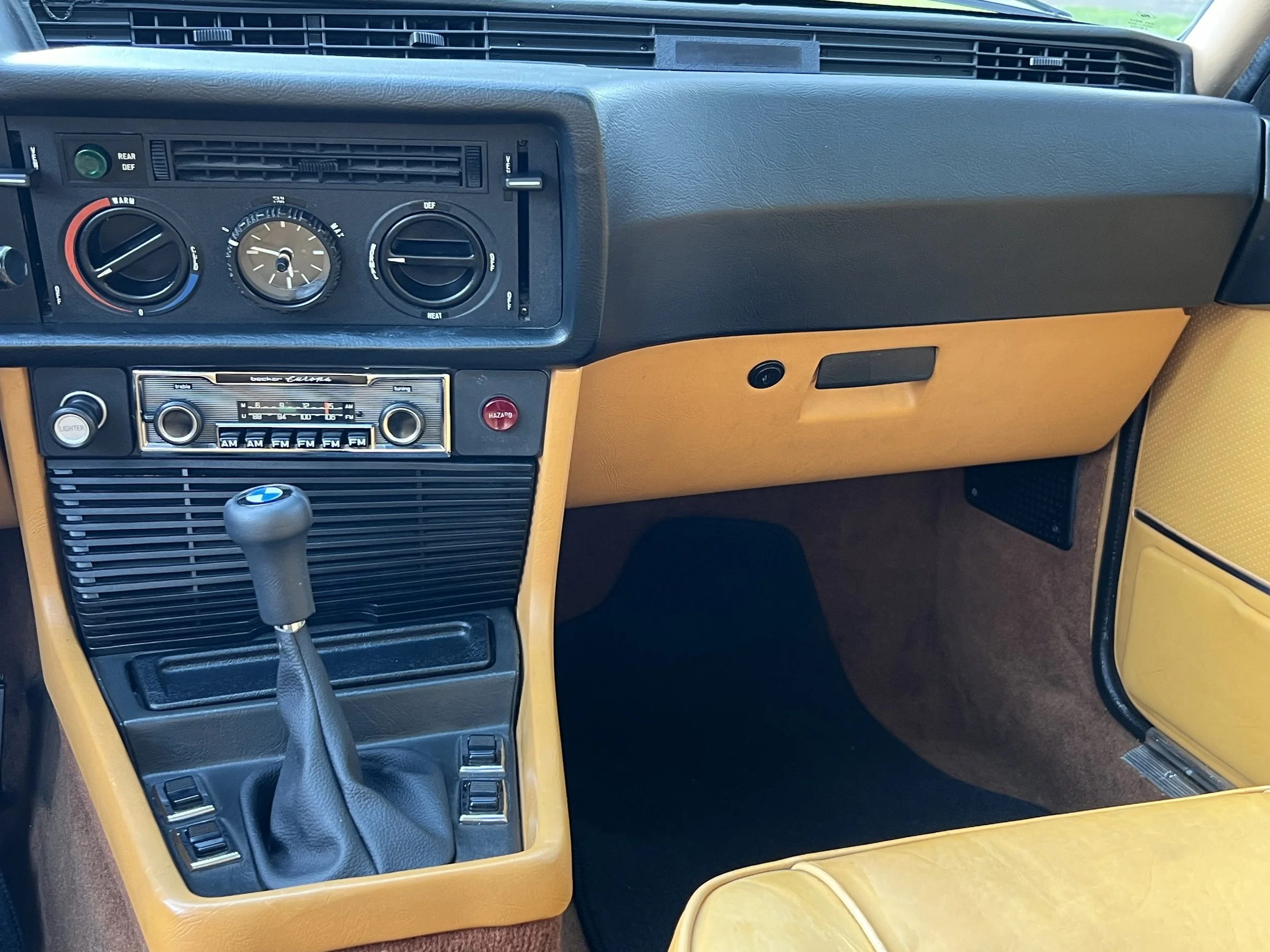 The interior of a vintage BMW BMW 630 csi car, showing the dashboard with air conditioning controls, radio, gear shift, and a yellow and black interior design.